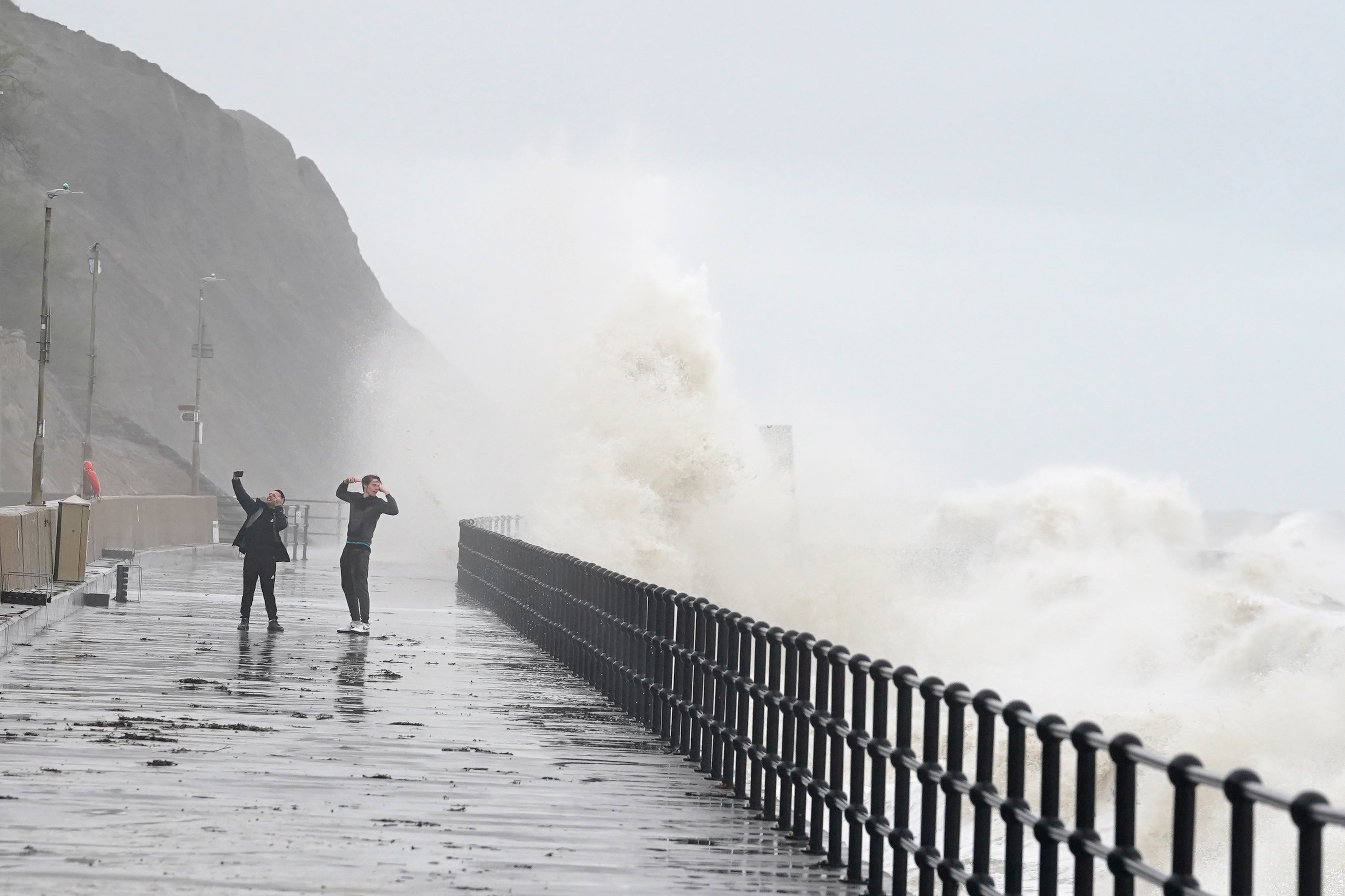 People photograph the waves crashing over the promenade in Folkestone, Kent