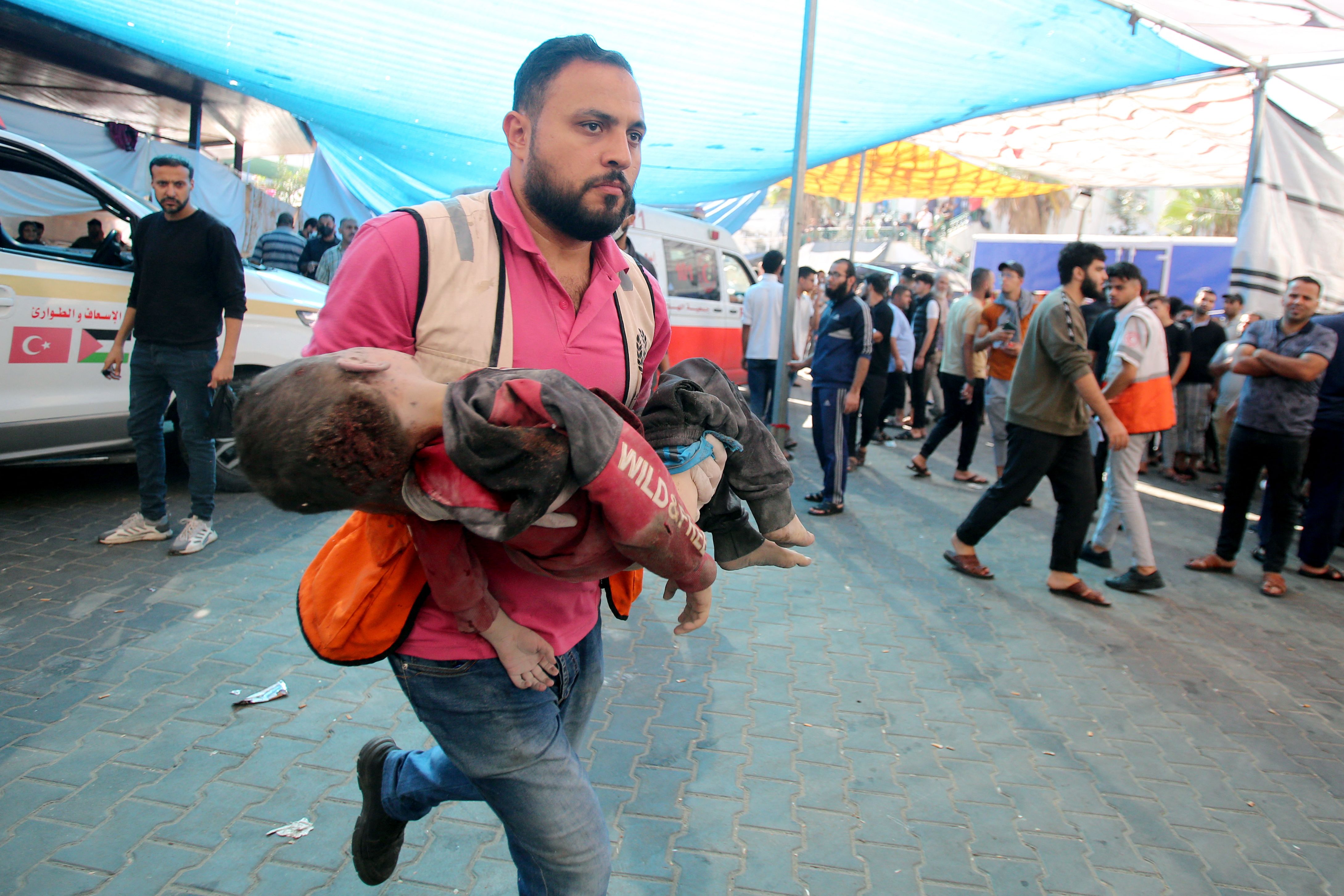 A man rushes with a toddler in his arms into Al-Shifa hospital in Gaza following Israeli bombing