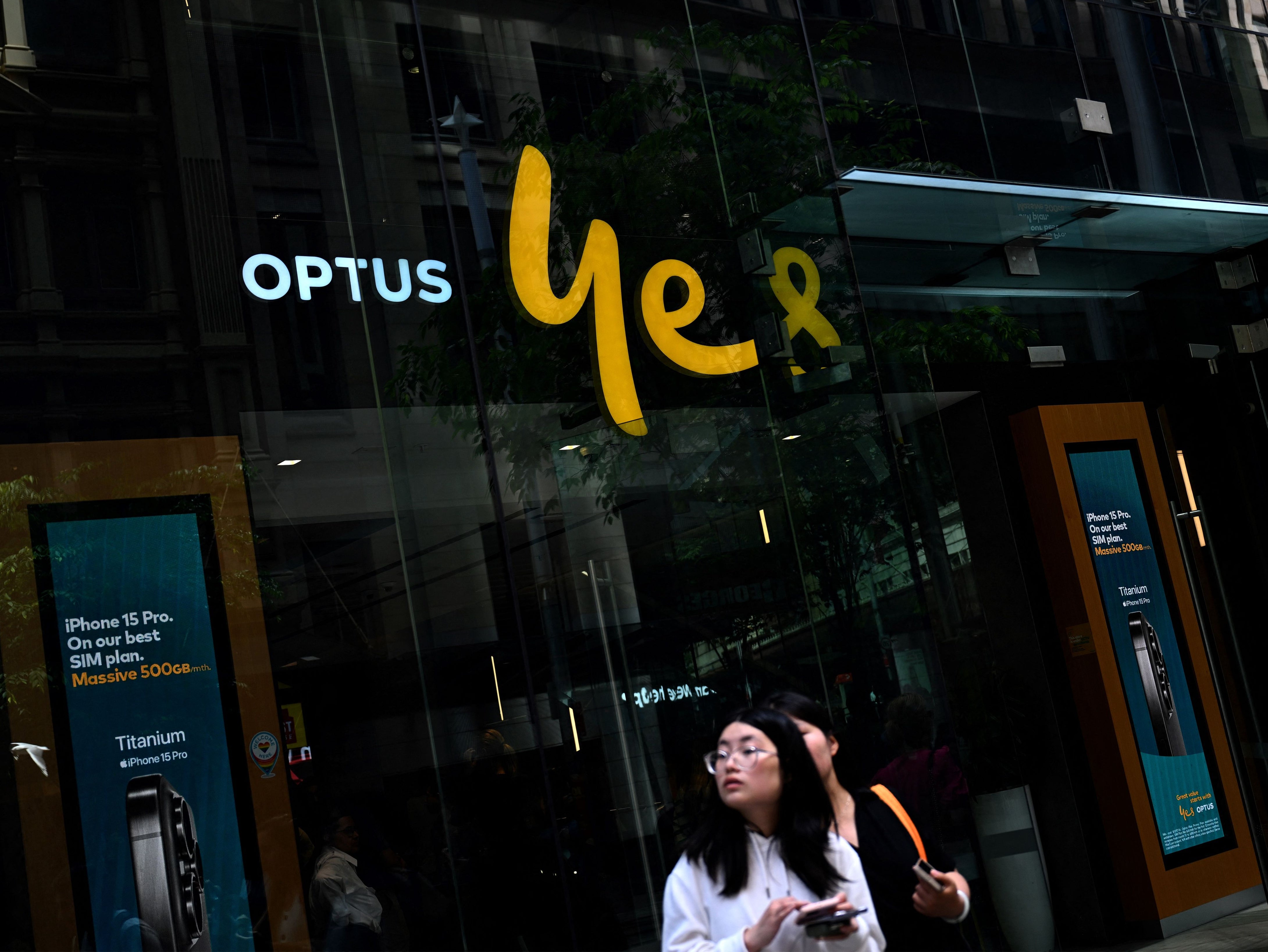 Girls browse on their mobile phones in front of Australian communications company Optus outlet in the central business district of Sydney on 8 November 2023