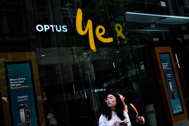 <p>Girls browse on their mobile phones in front of Australian communications company Optus outlet in the central business district of Sydney on 8 November 2023</p>