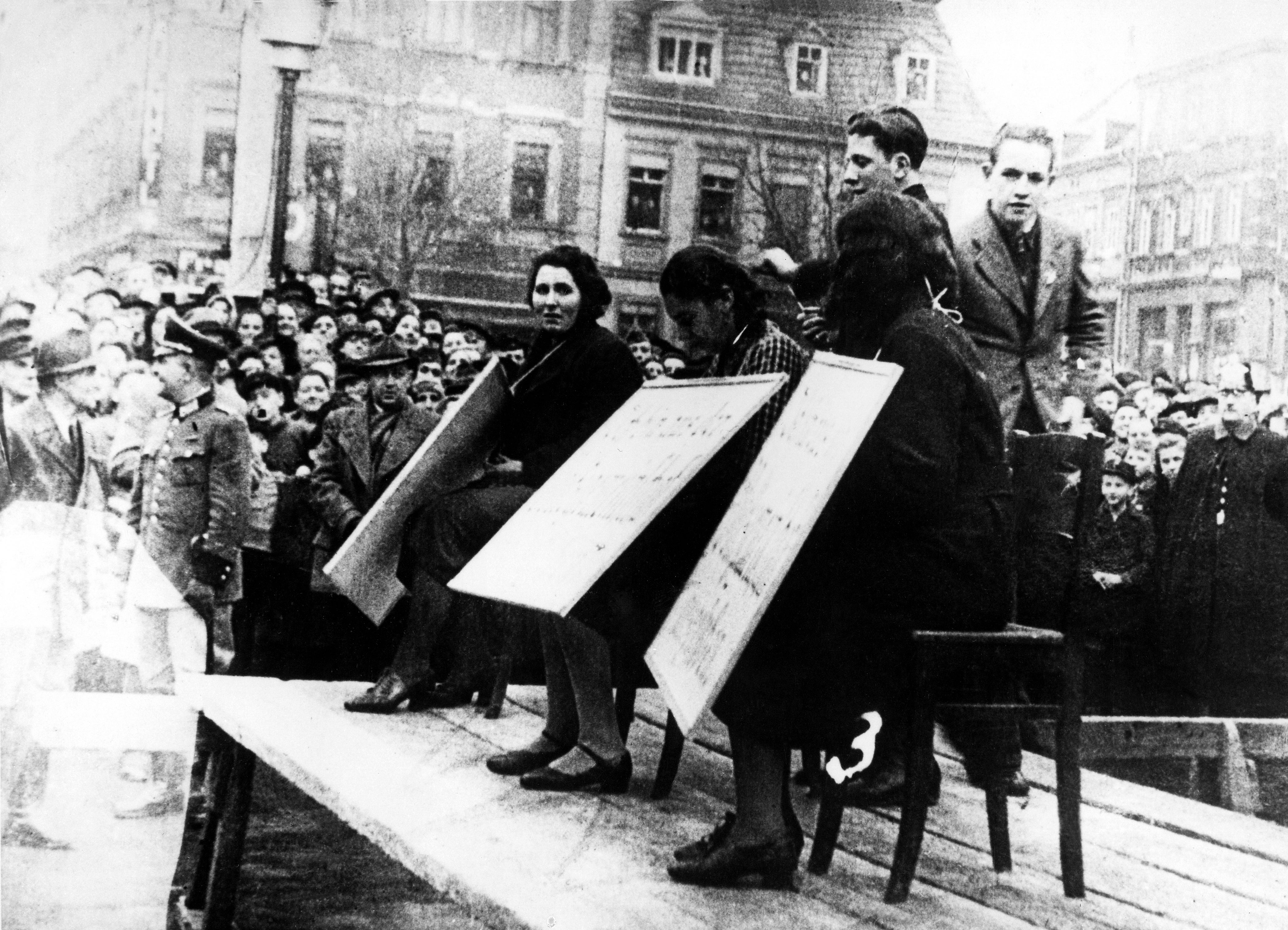 During the progroms Jewish women in Linz, Austria, are exhibited in public with a cardboard sign stating ‘I have been excluded from the national community (Volksgemeinschaft)’