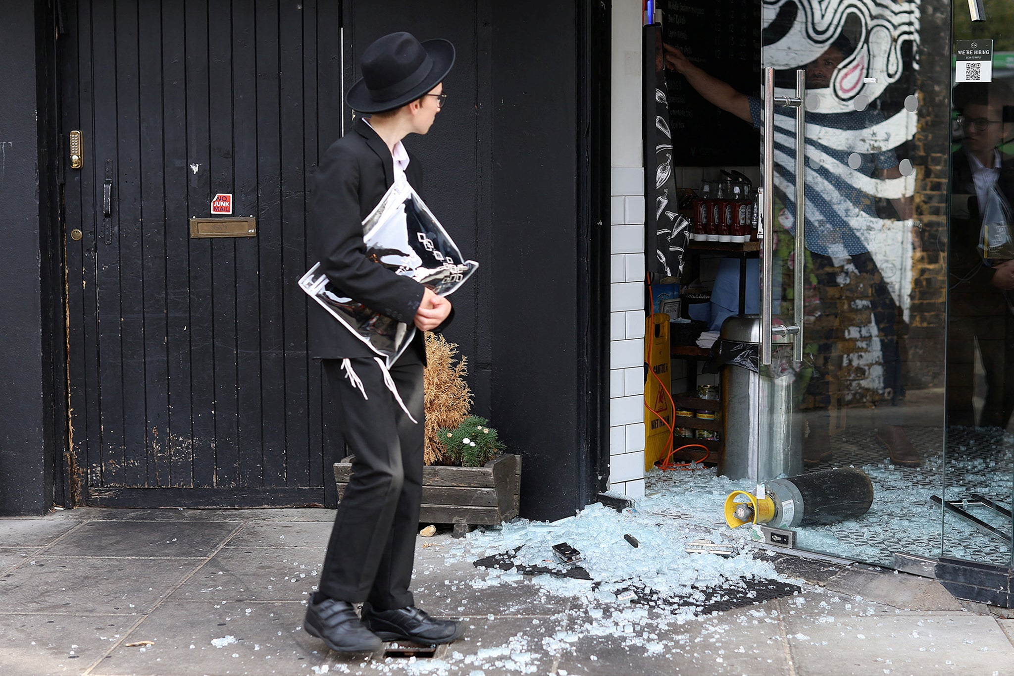 A man looks at a vandalised Kosher restaurant in Golders Green, London, near a bridge with ‘Free Palestine’ painted on it