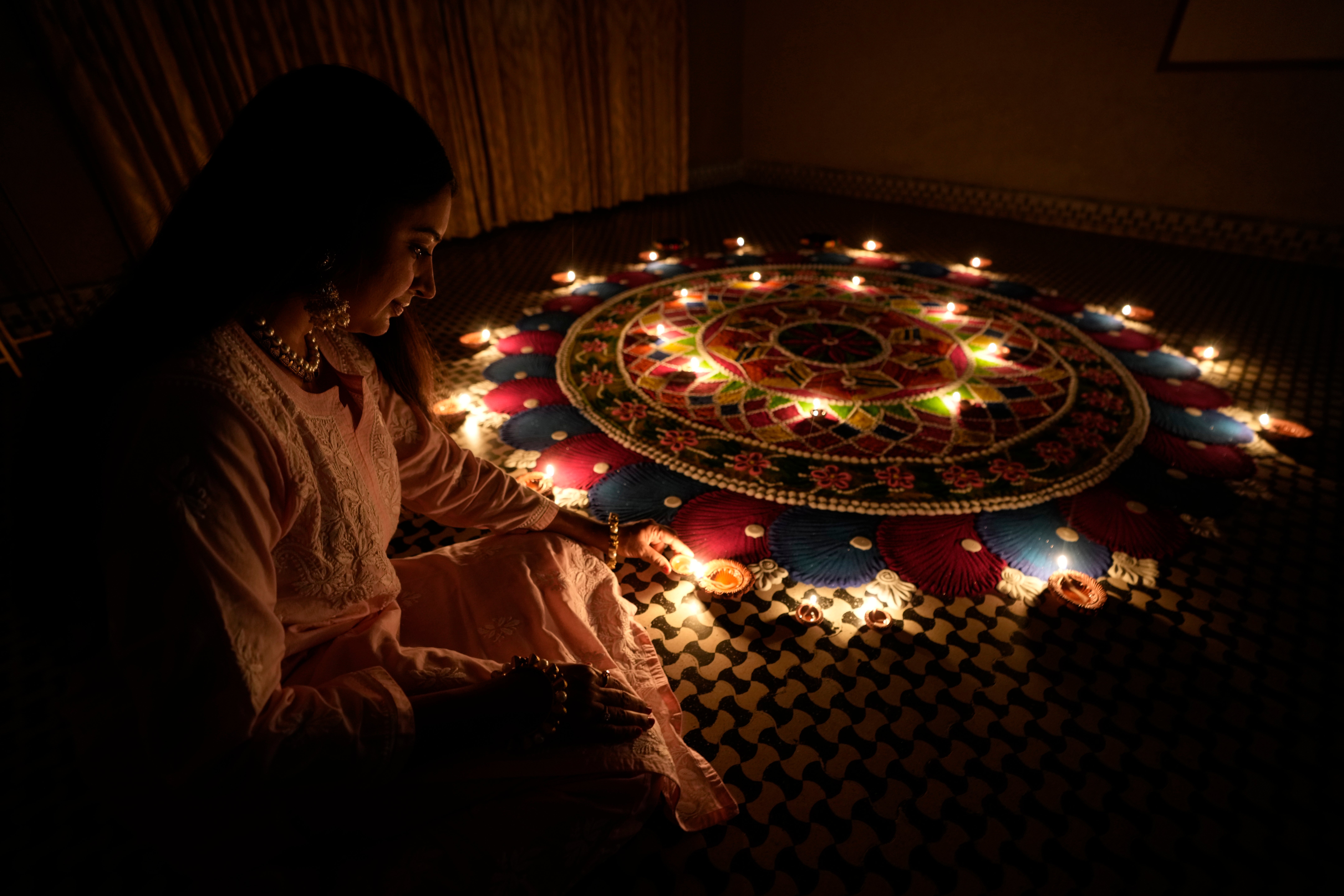 A girl lights an earthen lamp beside a rangoli, a hand decorated pattern on the floor, as part of Diwali festivities in Ahmedabad on 9 November