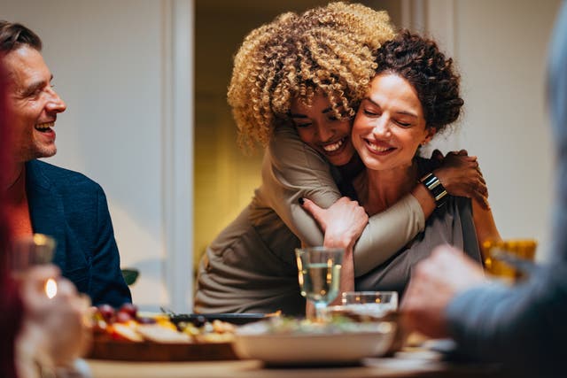 <p>Cheerful smiling African-American woman embracing her female friend during a dinner with family and friends.</p>