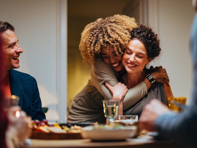 <p>Cheerful smiling African-American woman embracing her female friend during a dinner with family and friends.</p>