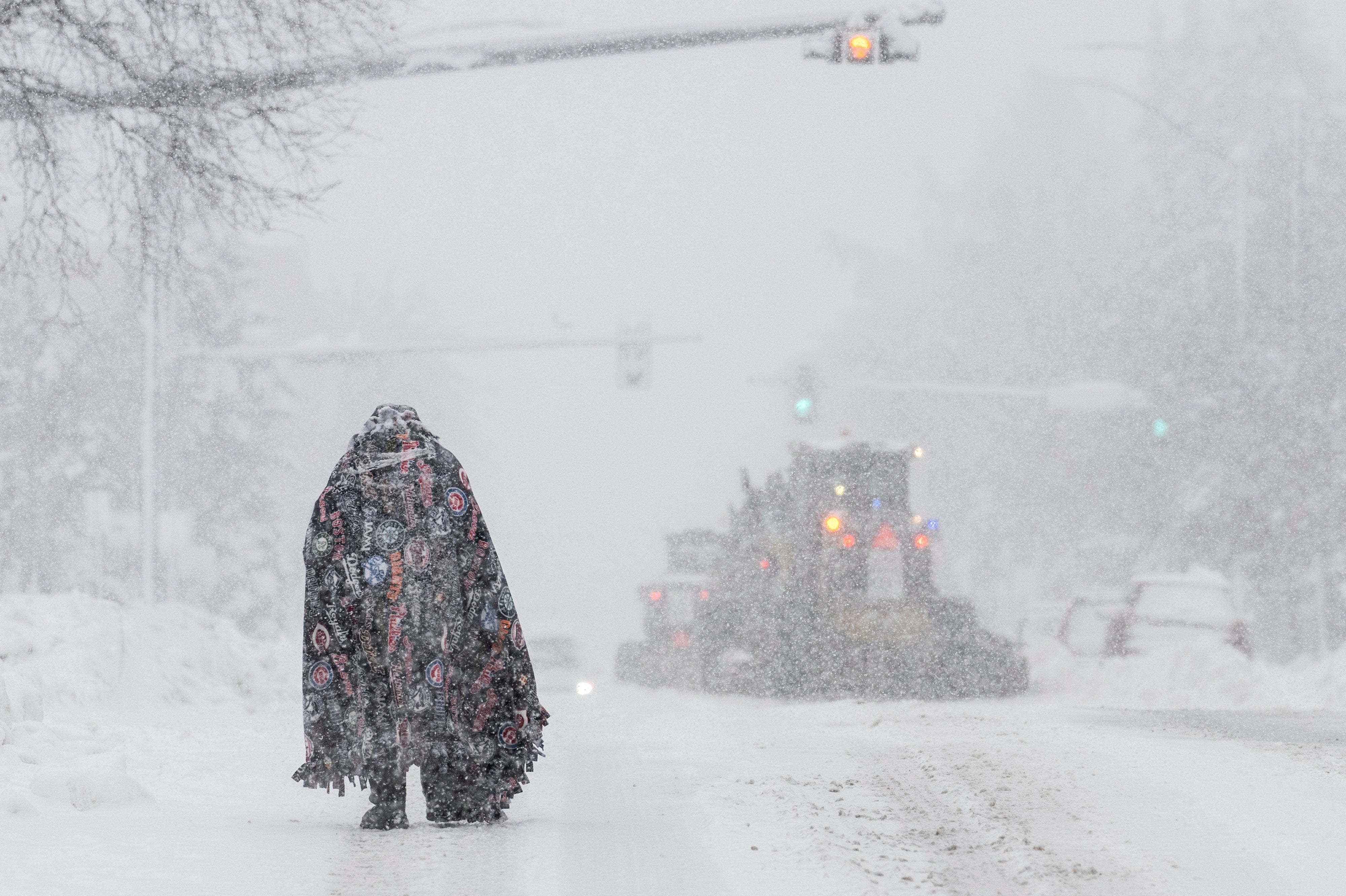 A pedestrian takes cover under a blanket in Anchorage as plows clear the roadway on 9 November