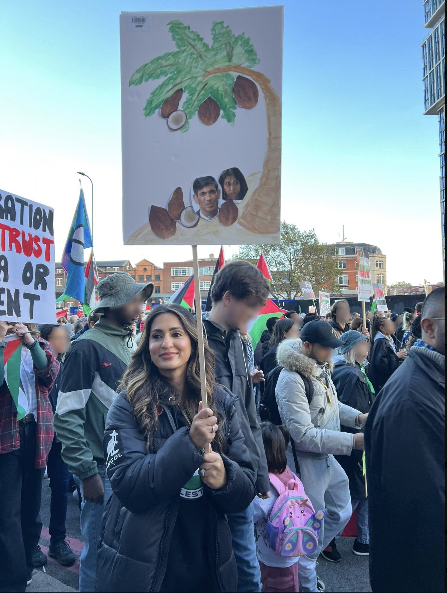Police are also investigating the woman pictured here who held a placard depicting a palm tree with Suella Braverman and Rishi Sunak below as fallen coconuts