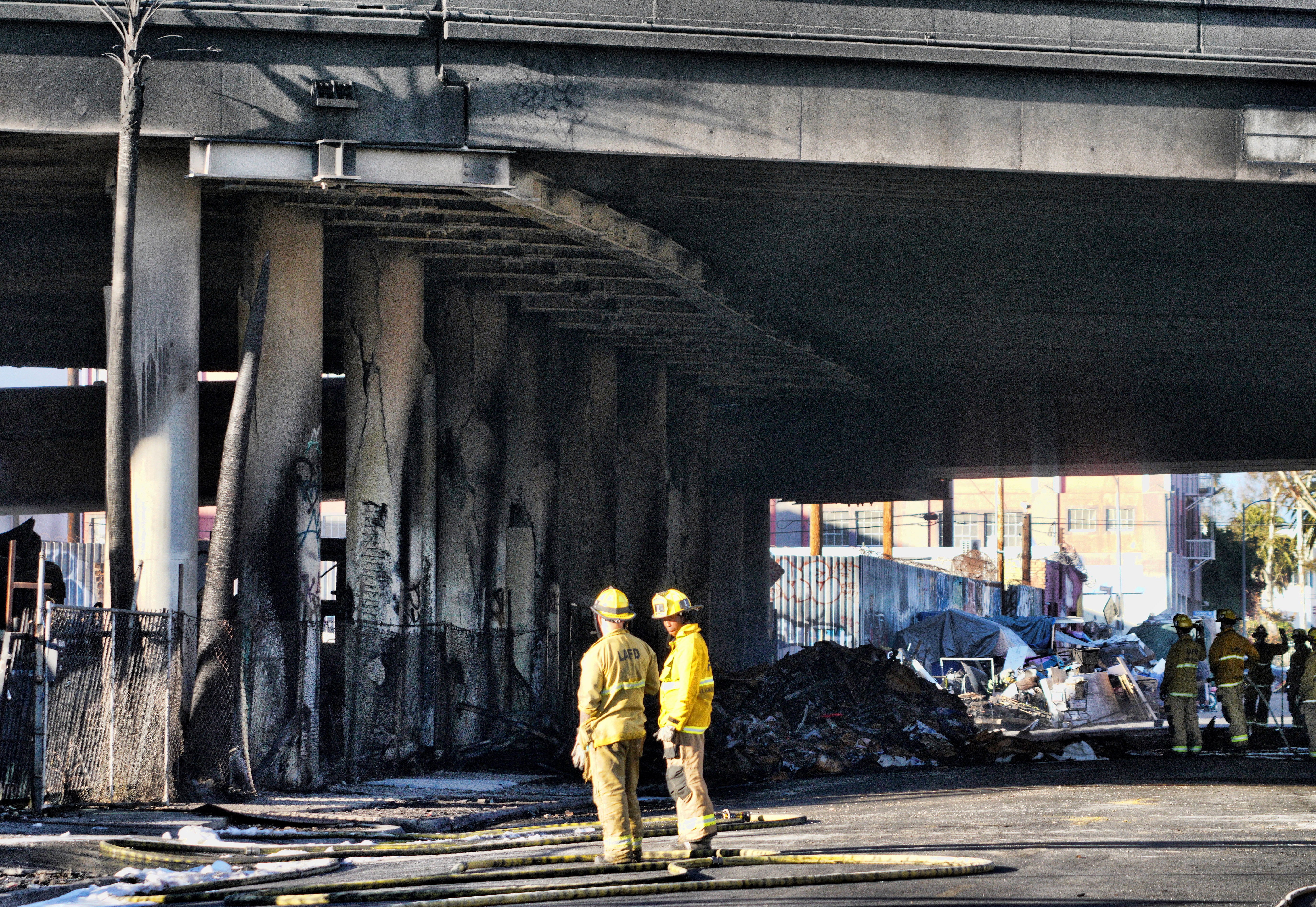 Firefighters assess the damage from a intense fire under Interstate 10 that severely damaged the overpass in an industrial zone near downtown Los Angeles on Saturday