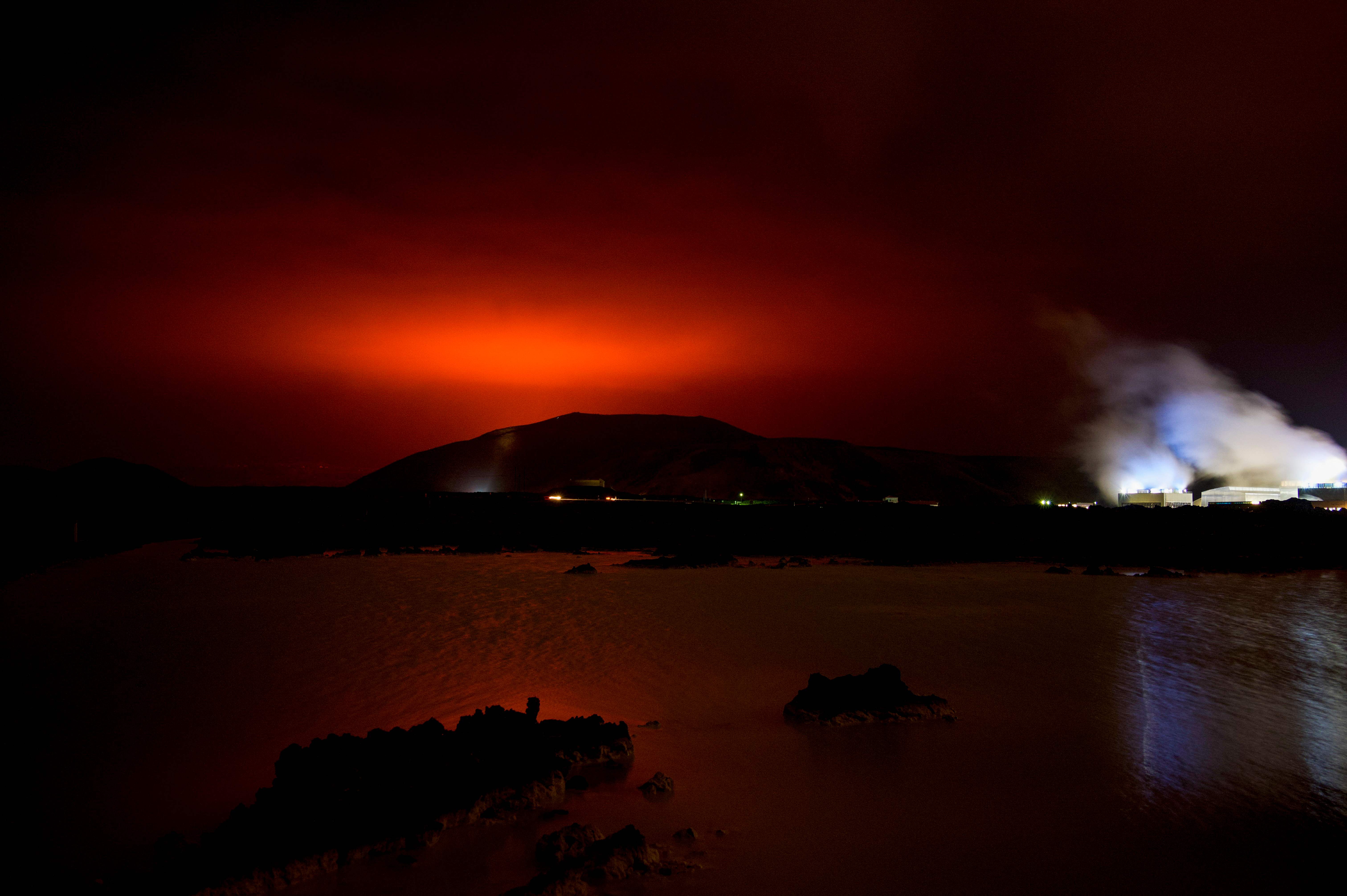 <p>The red shimmer from magma flowing out from the erupting Fagradalsfjall volcano behind the landmark Blue Lagoon, some 45 km west of the Icelandic capital Reykjavik, on 19 March 2021</p>