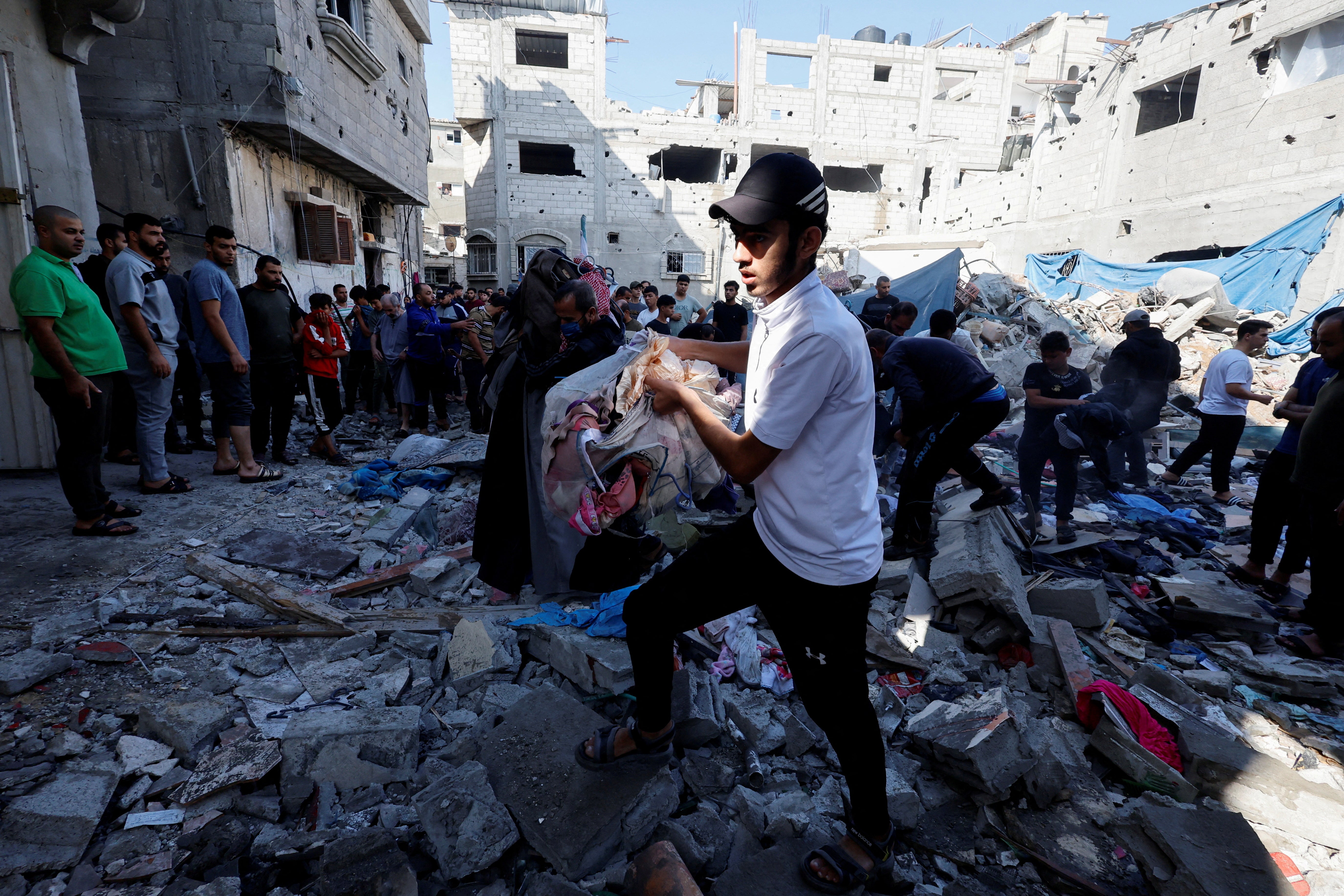 A Palestinian man carries objects as he walks through debris on 14 November in the aftermath of an Israeli strike in Gaza