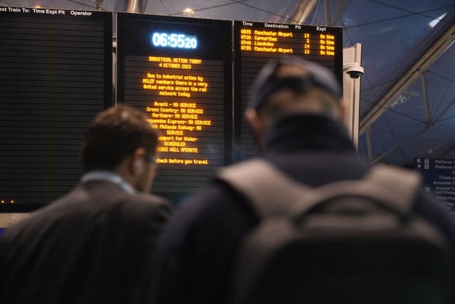 Commuters stand in front of an information sign detailing strike action at Manchester Piccadilly train station (PA)