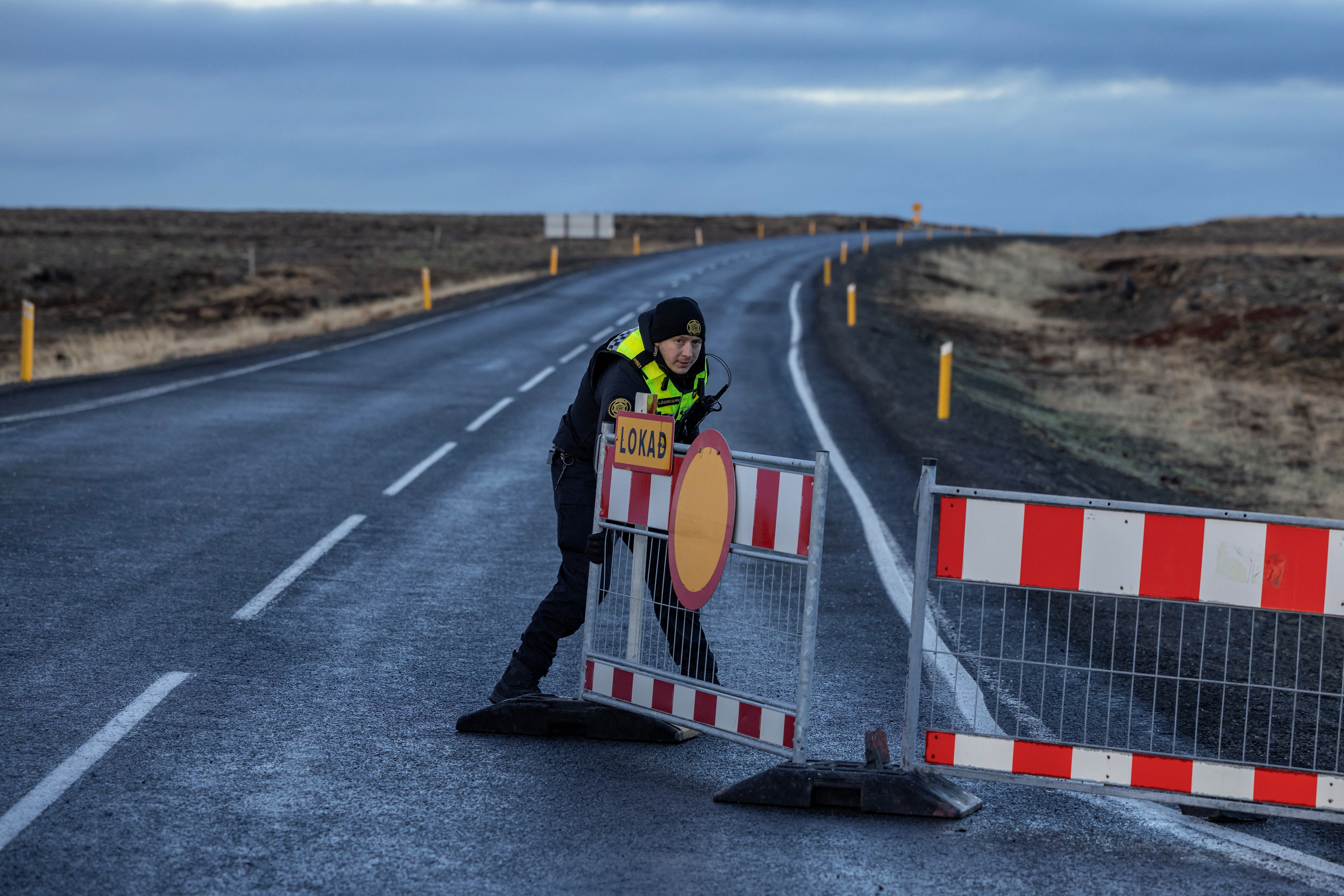 A police officer pulls a barrier to block the road leading to the fishing town of Grindavik,