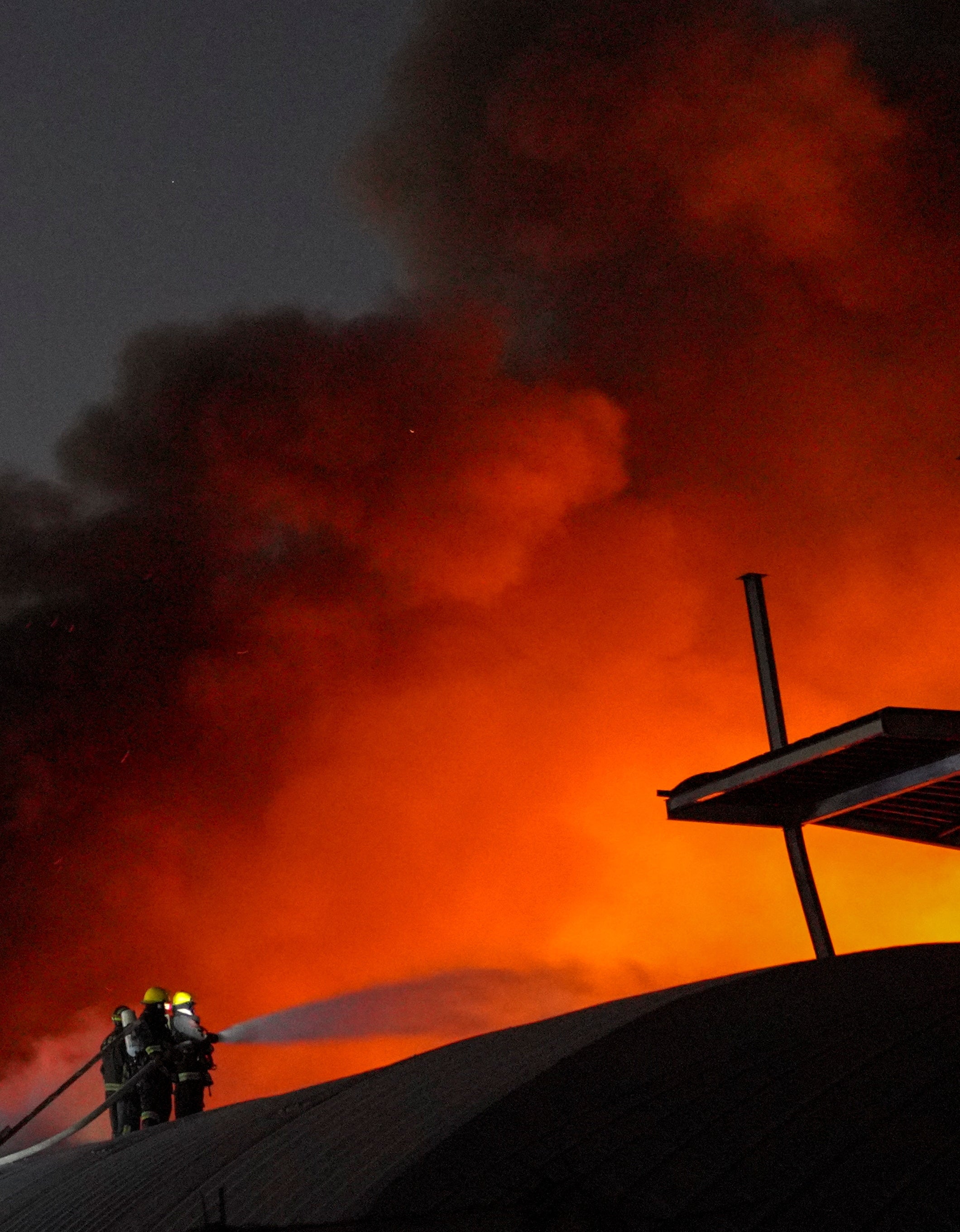 Firefighters try to douse the fire as smoke and fire rise out of a shoe warehouse