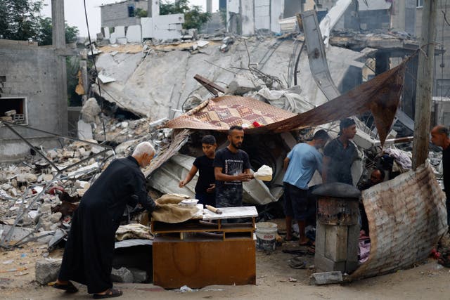 <p>Palestinians prepare food next to destroyed buildings following Israeli strikes on Khan Younis in the southern Gaza Strip</p>