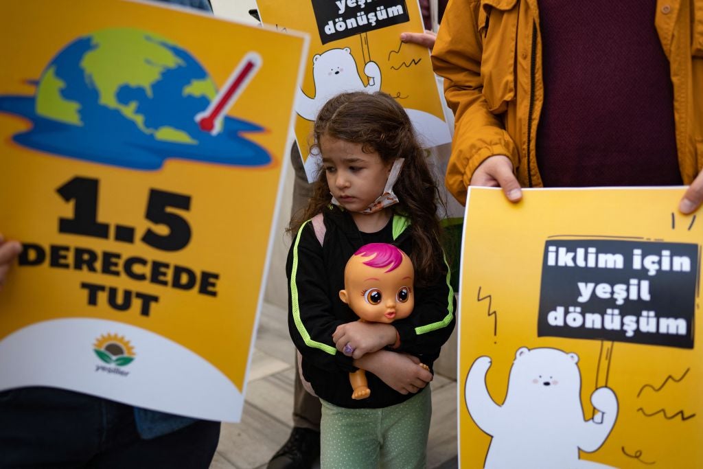 A young girl holding a babydoll stands between placards during a protest rally as part of a global day of action on climate change in Istanbul, on November 6, 2021