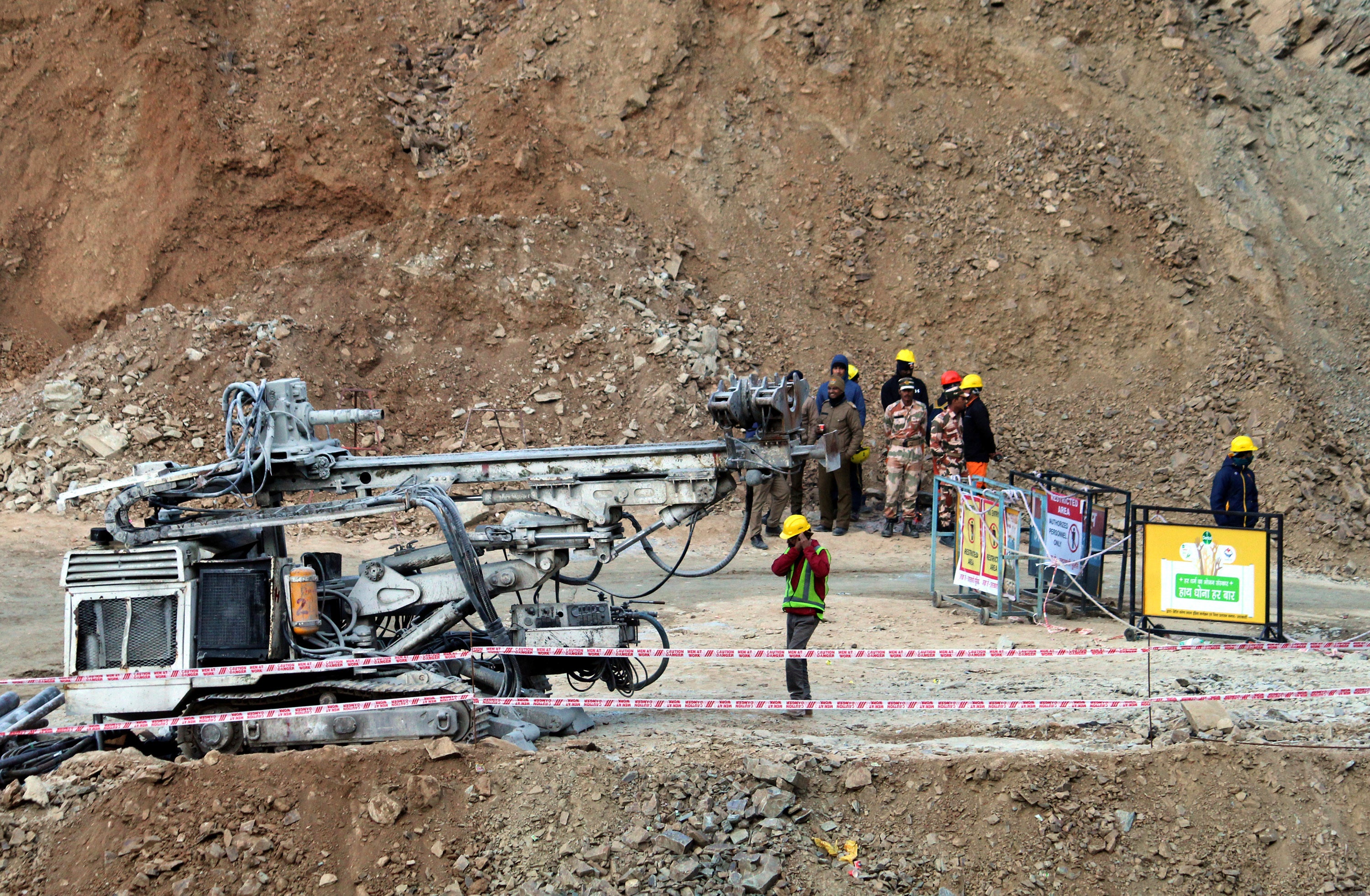 Rescuers stand near heavy machinery at the site of an under-construction road tunnel that collapsed in mountainous Uttarakhand state