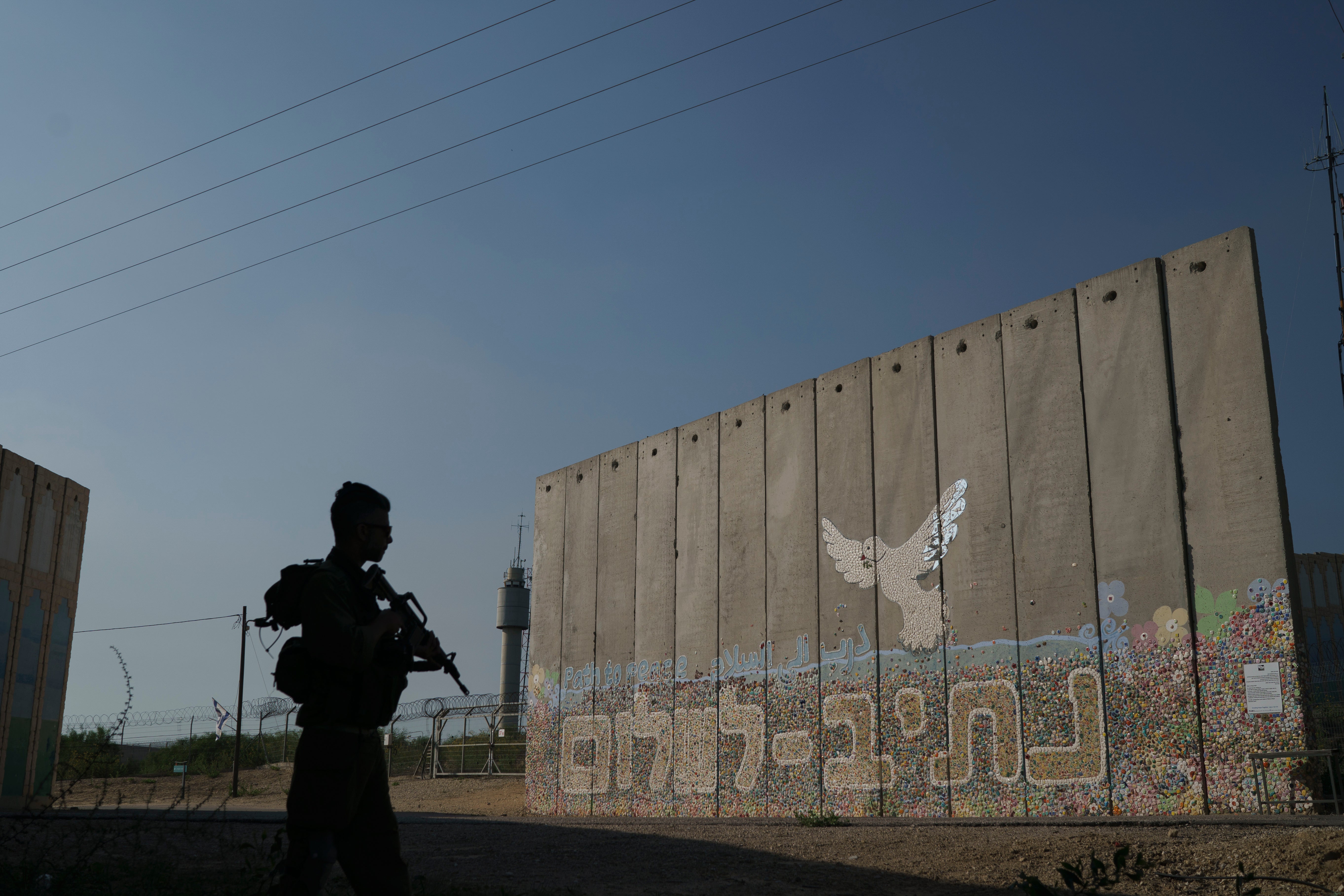 A member of Israeli forces stands next to a security wall with Hebrew writing reading ‘Path to Peace’ at the Kibbutz Netiv HaAsara, near the border with Gaza Strip, in November 2023