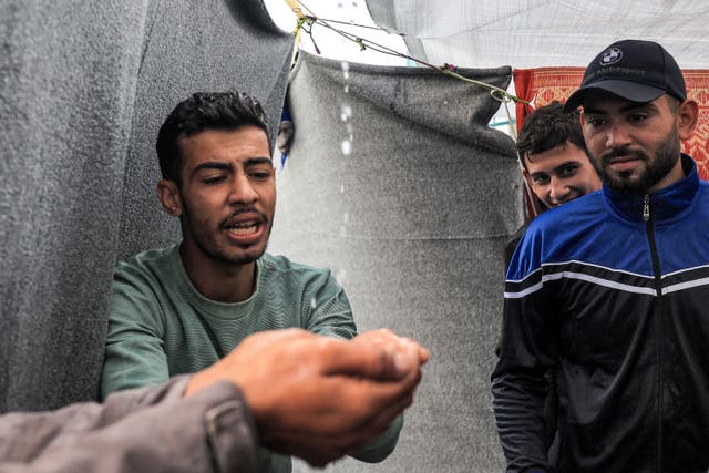 <p>Men use their hands to drink rainwater dripping from the roof of a tent amid water shortages while at a school run by the United Nations Relief and Works Agency for Palestine Refugees in the Near East (UNRWA) in Rafah on 14 November 2023</p>