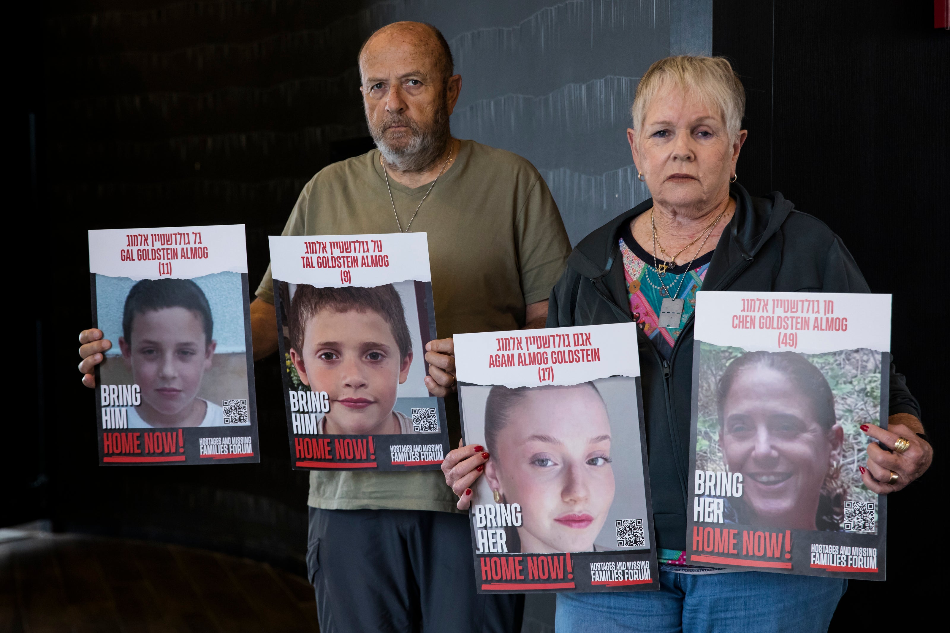 David and Varda Goldstein pose for a picture whilst holding-up photos of their 3 grandchildren, Gal, Tal and Agam, and their mother, Chen, who were kidnapped by Hamas