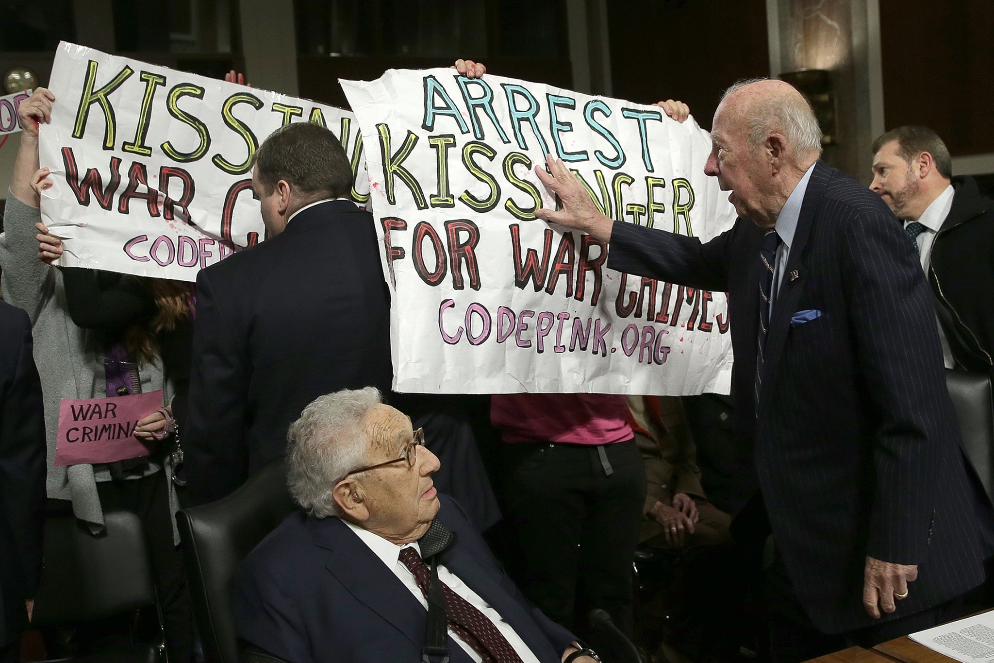 Former US Secretary of State George Shultz (C) pushes away protesters shouting "Arrest Henry Kissinger for war crimes" as former U.S. Secretary of State Henry Kissinger (L) watches prior to the two testifying before the Senate Armed Services Committee 29 January 2015 in Washington, DC.