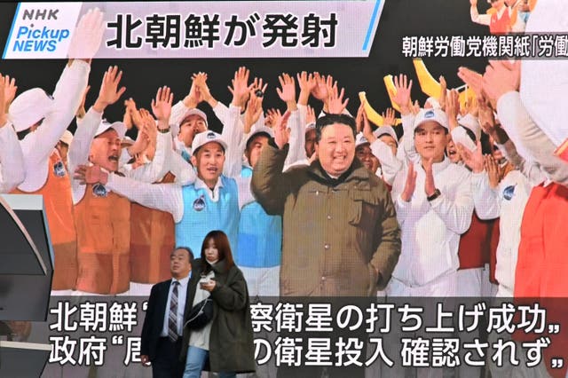 <p>Pedestrians walk past a screen displaying North Korea's leader Kim Jong Un (C) celebrating after the reconnaissance satellite 'Malligyong-1' was launched</p>