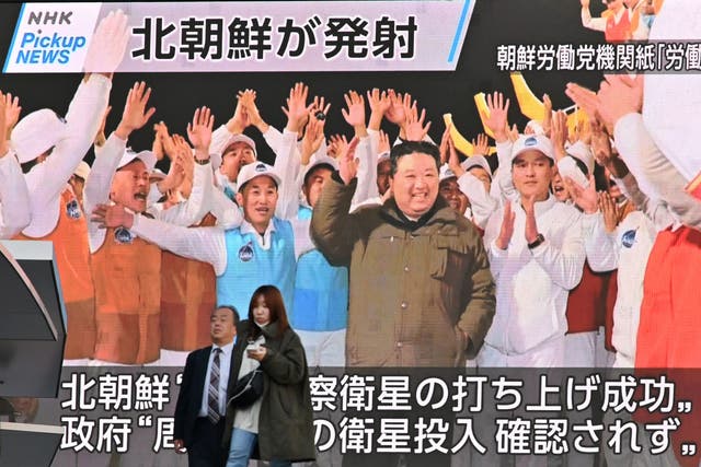 <p>Pedestrians walk past a screen displaying North Korea's leader Kim Jong Un (C) celebrating after the reconnaissance satellite 'Malligyong-1' was launched</p>