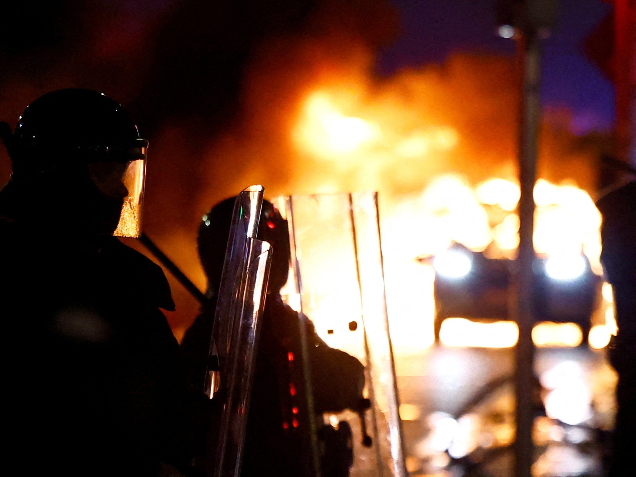 Riot police stand next to a burning police vehicle during a demonstration following a suspected stabbing that left children injured in Dublin, Ireland on Thursday