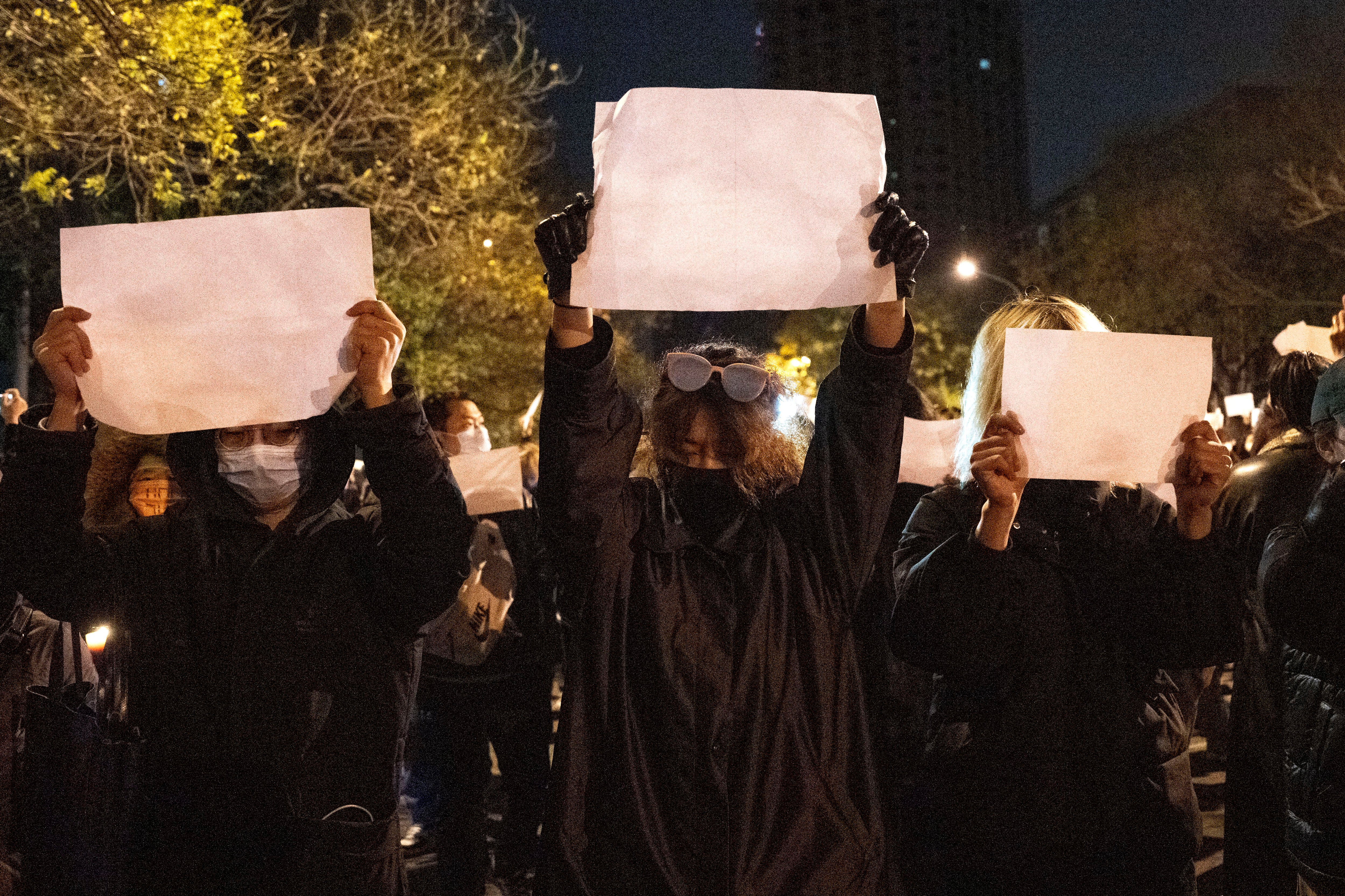 Protesters hold up blank pieces of paper and chant slogans as they march to protest strict anti-virus measures in Beijing