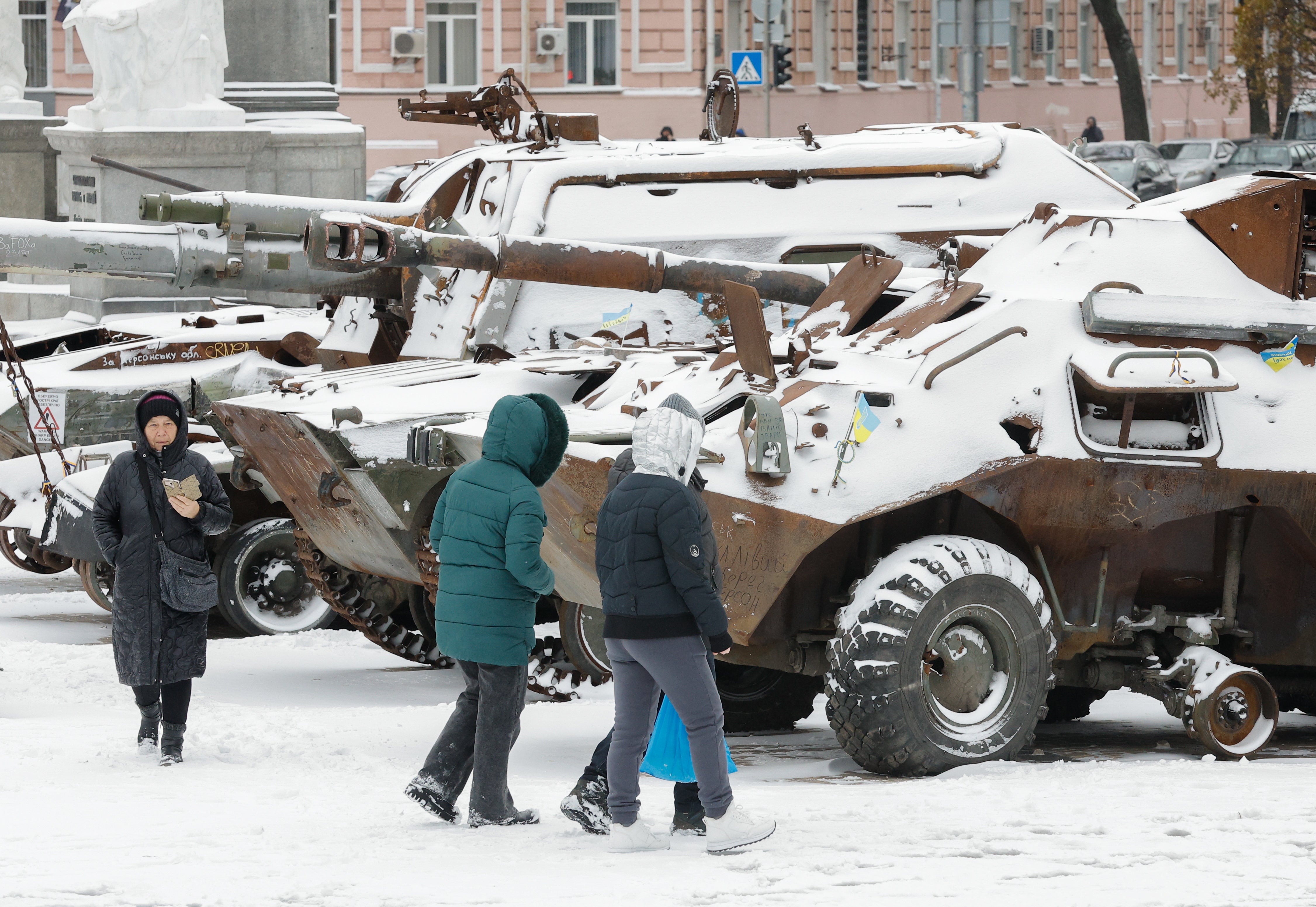 People walk past snow covered, destroyed Russian machinery displayed in Kyiv