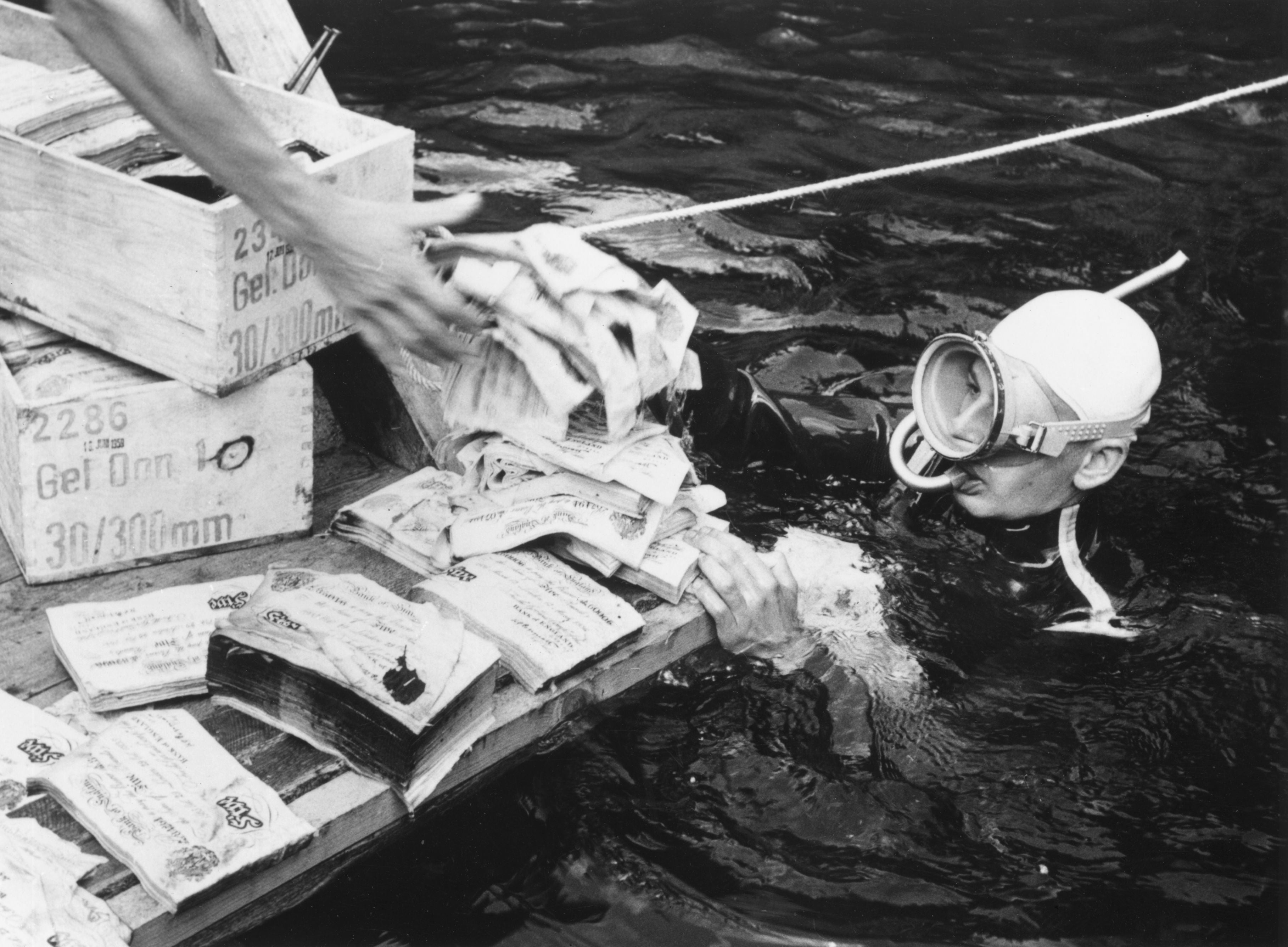 A scuba diver passes forged £5 notes from Lake Toplitz. The notes were forged by the Nazis in an attempt to destabilise the British economy but were dumped in the lake at the end of the conflict