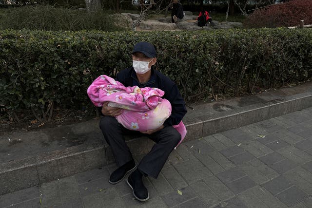 <p>A man carrying a child sits outside a children's hospital in Beijing</p>