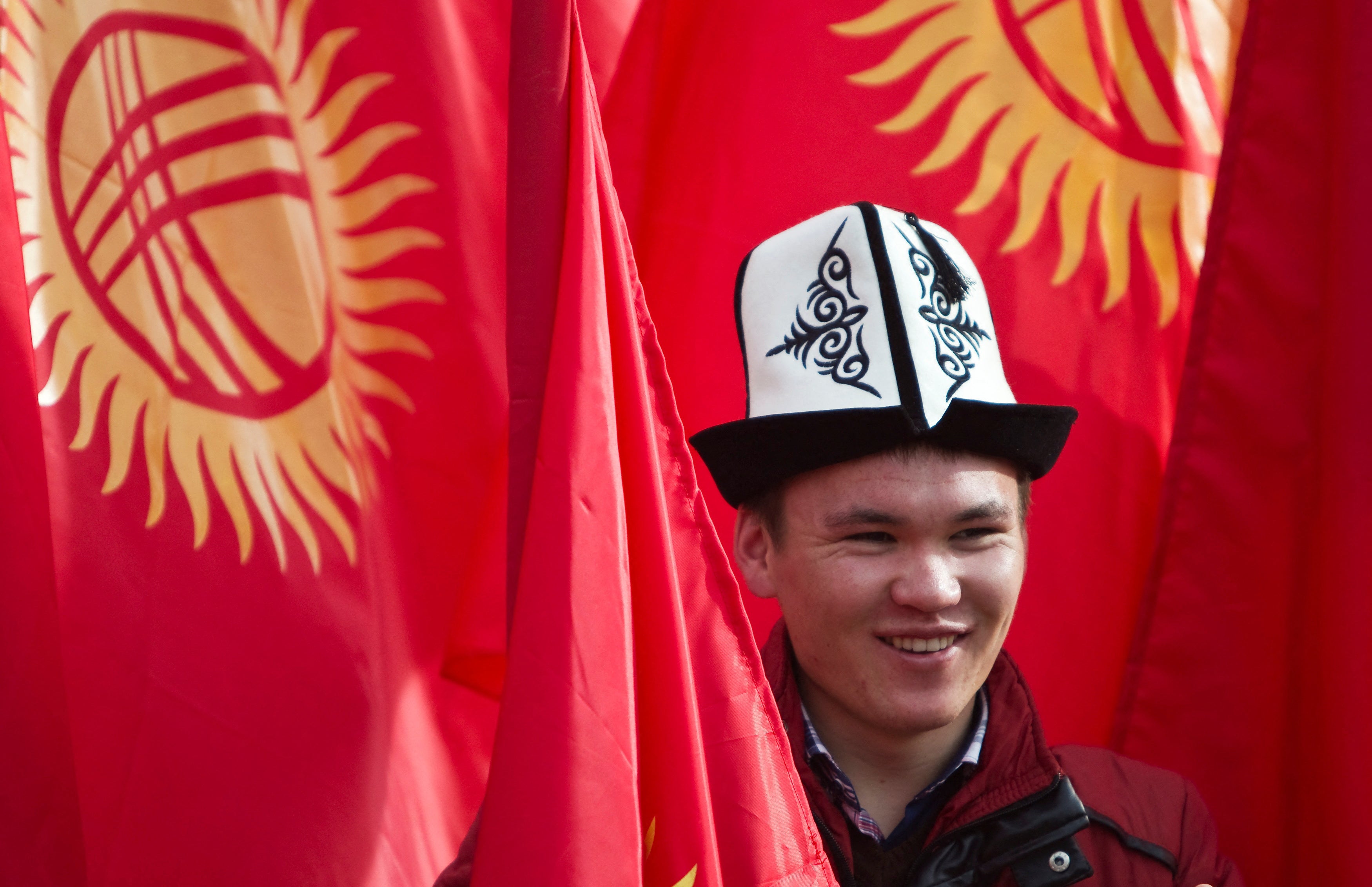 A man wearing a Kyrgyz national hat poses with national flags before a rally marking the Day of Flag and the Day of Kolpak in Bishkek, Kyrgyzstan