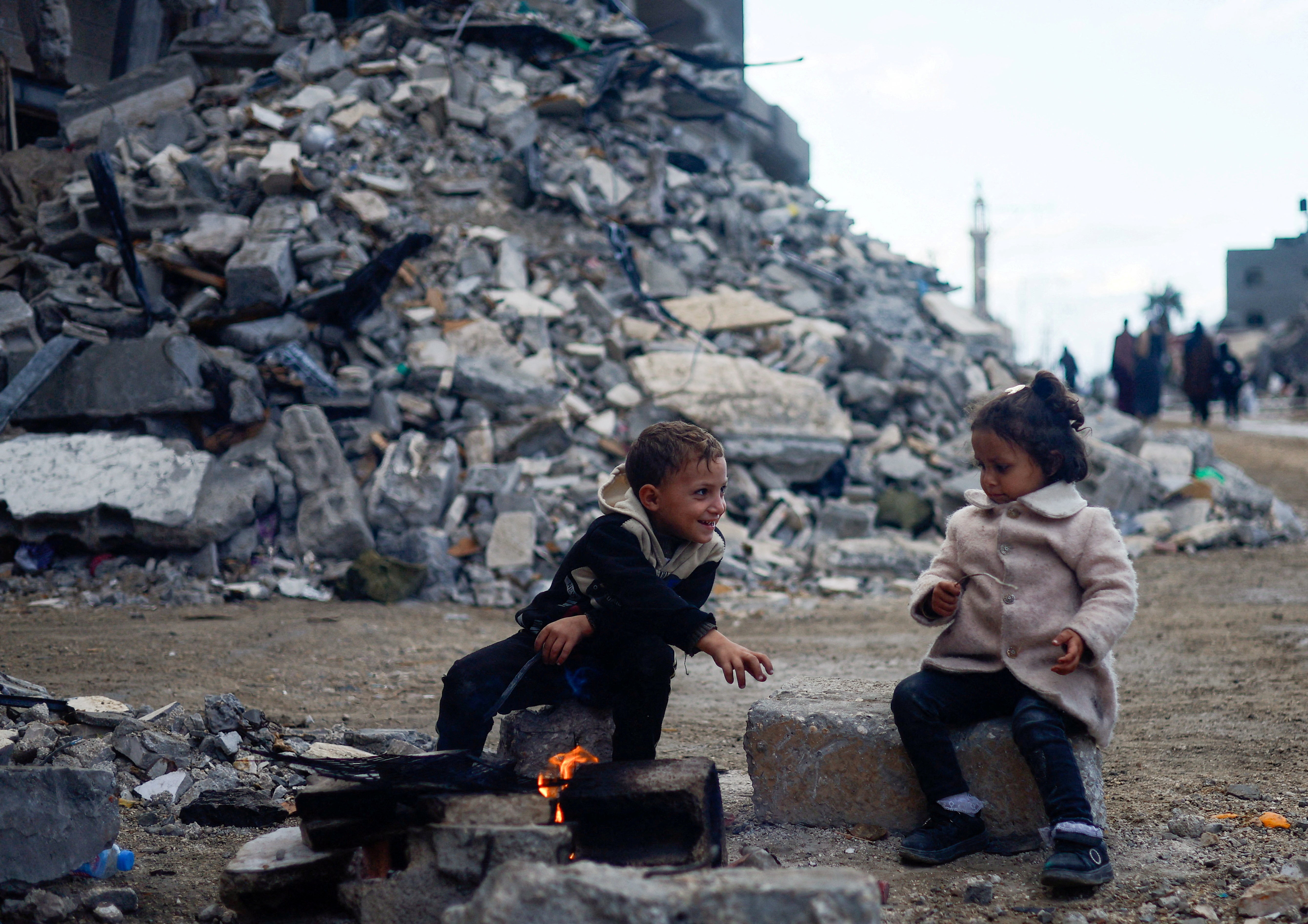 Palestinian children sit by the fire next to the rubble of a house, in Khan Younis