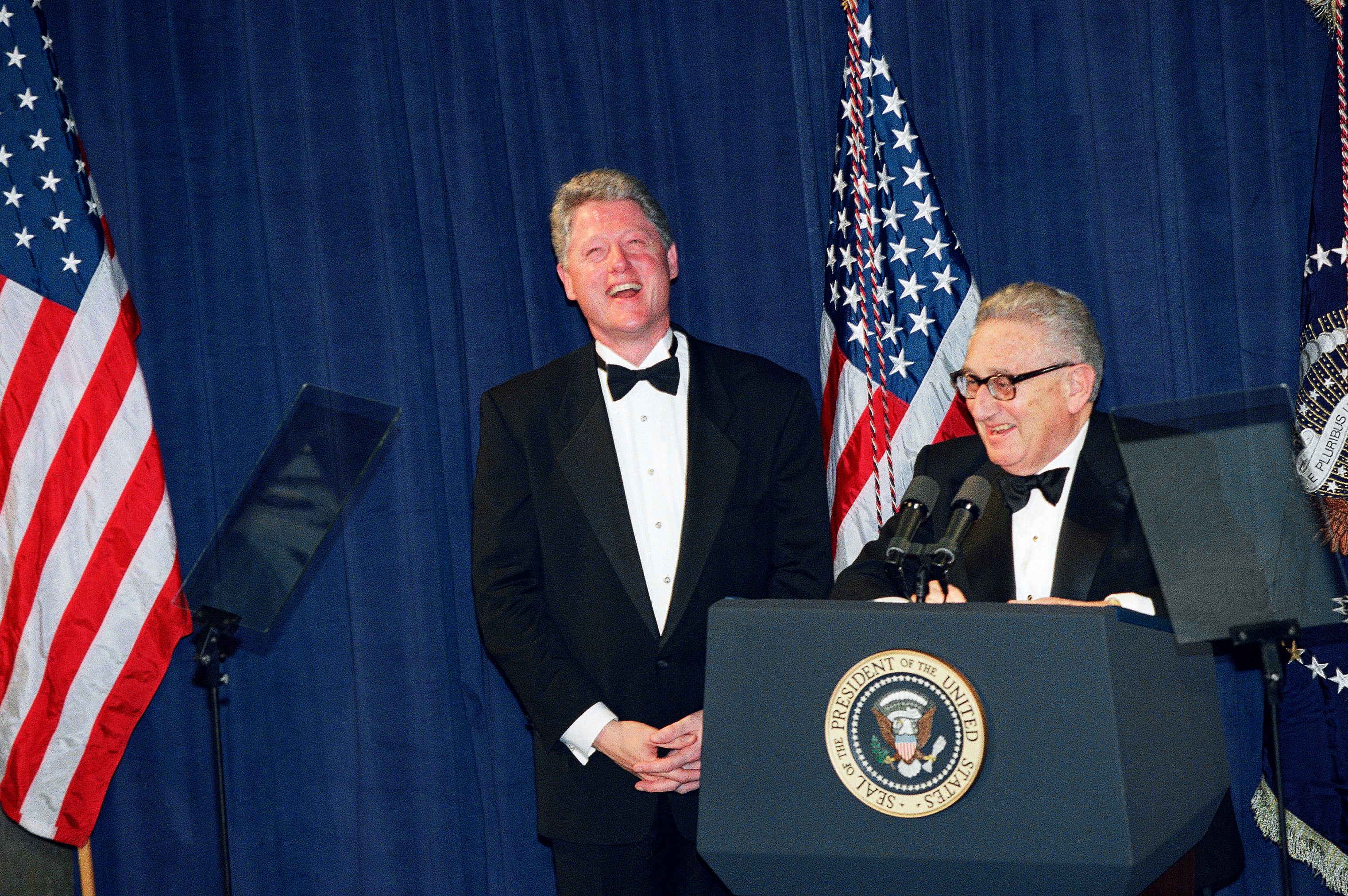 President Bill Clinton, left, and former Secretary of State Henry Kissinger laugh at a national policy conference, March 1, 1995