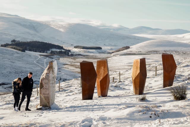 <p>A couple walk past The Watchers Art Instillation and A Moment in Time at Corgarff view, Scotland </p>