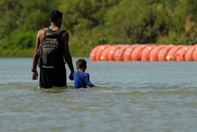 <p>Migrants walk past large buoys being used as a floating border barrier on the Rio Grande, Aug. 1, 2023, in Eagle Pass, Texas</p>