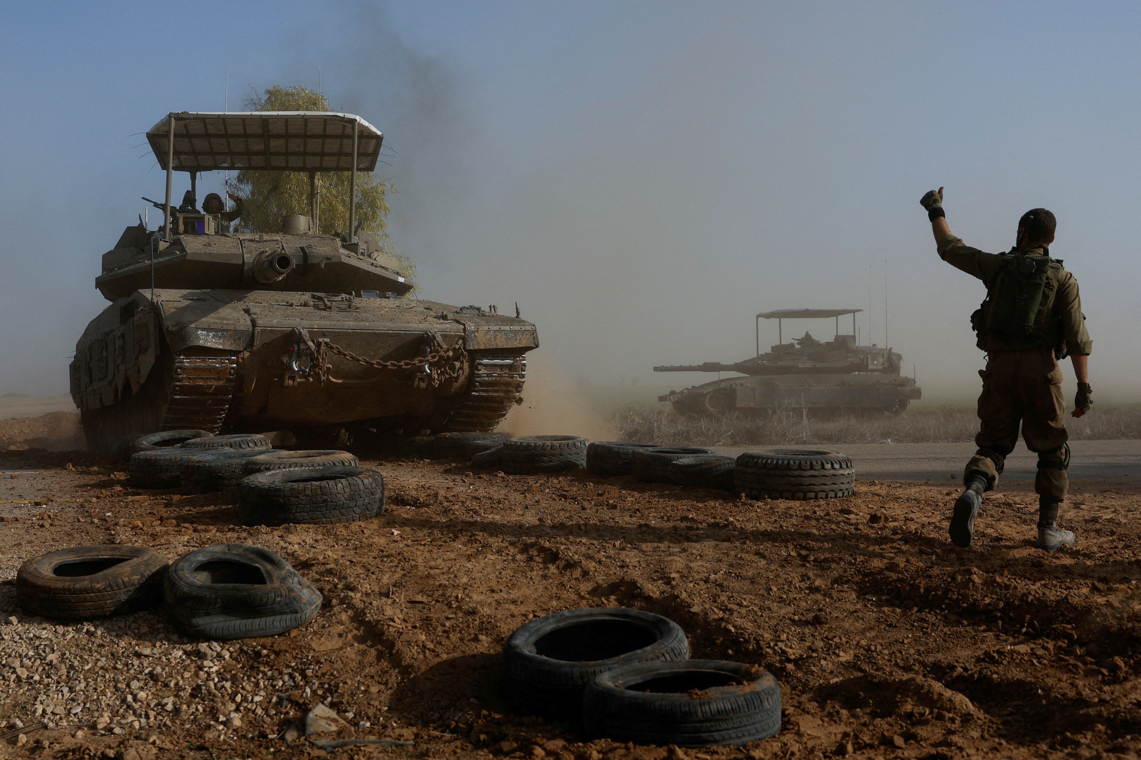 An Israeli soldier gestures towards a tank crew member as it crosses a road