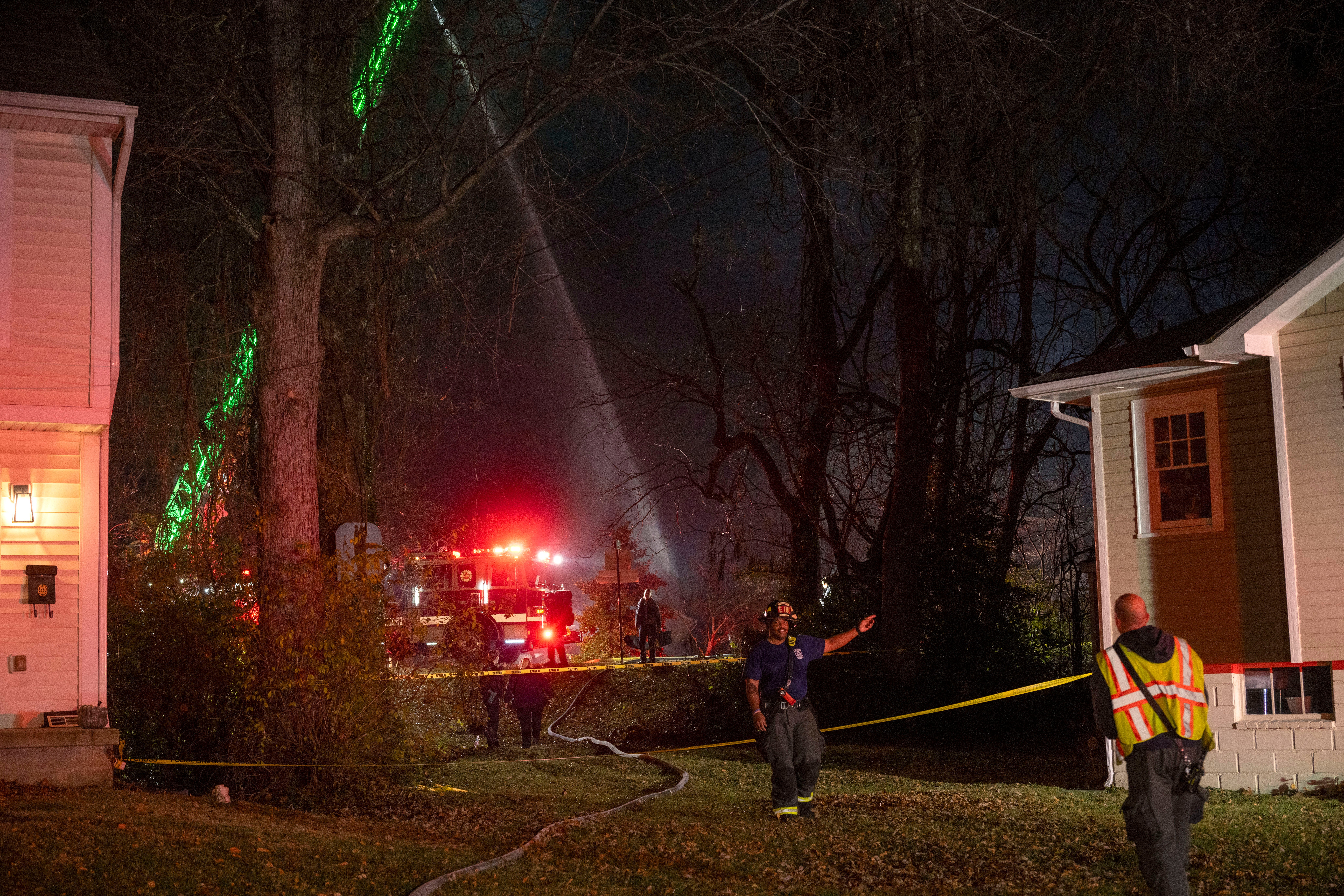 Fire and police officials walk around the scene of a house explosion as an Arlington County Fire Department ladder truck sprays water down on the remains of the building on Monday, Dec. 4, 2023, in Arlington, Va.