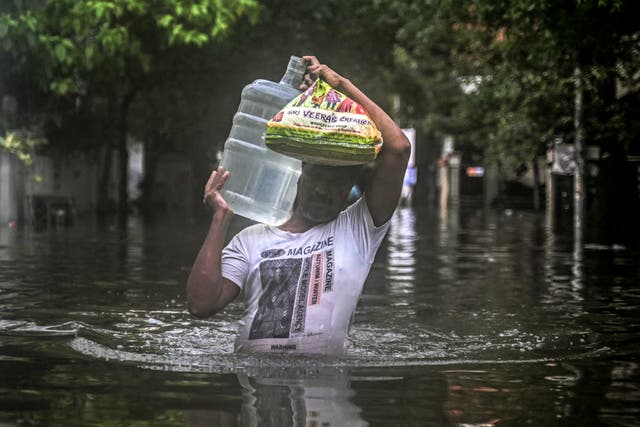 <p>A man carrying drinking water wades along a flooded street in Chennai on December 5, 2023, following intense rains after Cyclone Michaung made a landfall</p>