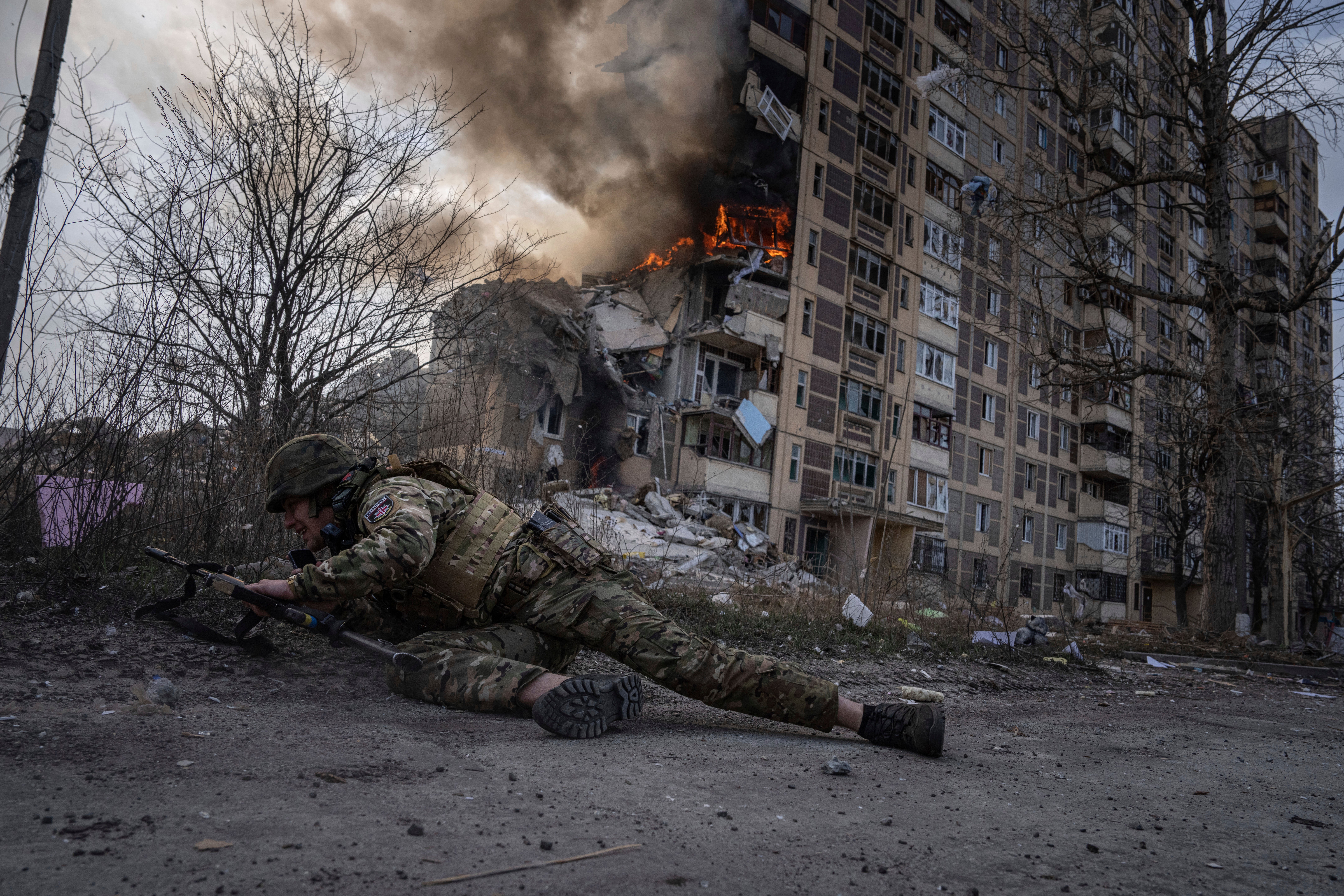 A police officer takes cover in front of a burning building that was hit in a Russian airstrike in Avdiivka, eastern Ukraine