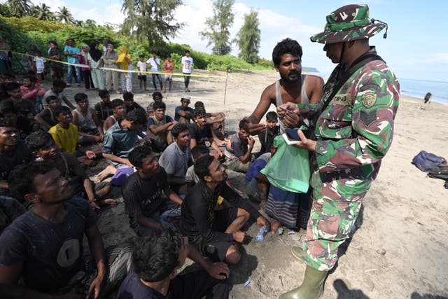 <p>An Indonesian soldier inspects the identification of ethnic Rohingya men after they land on a beach in Pidie, Aceh province, on Sunday 10 December </p>