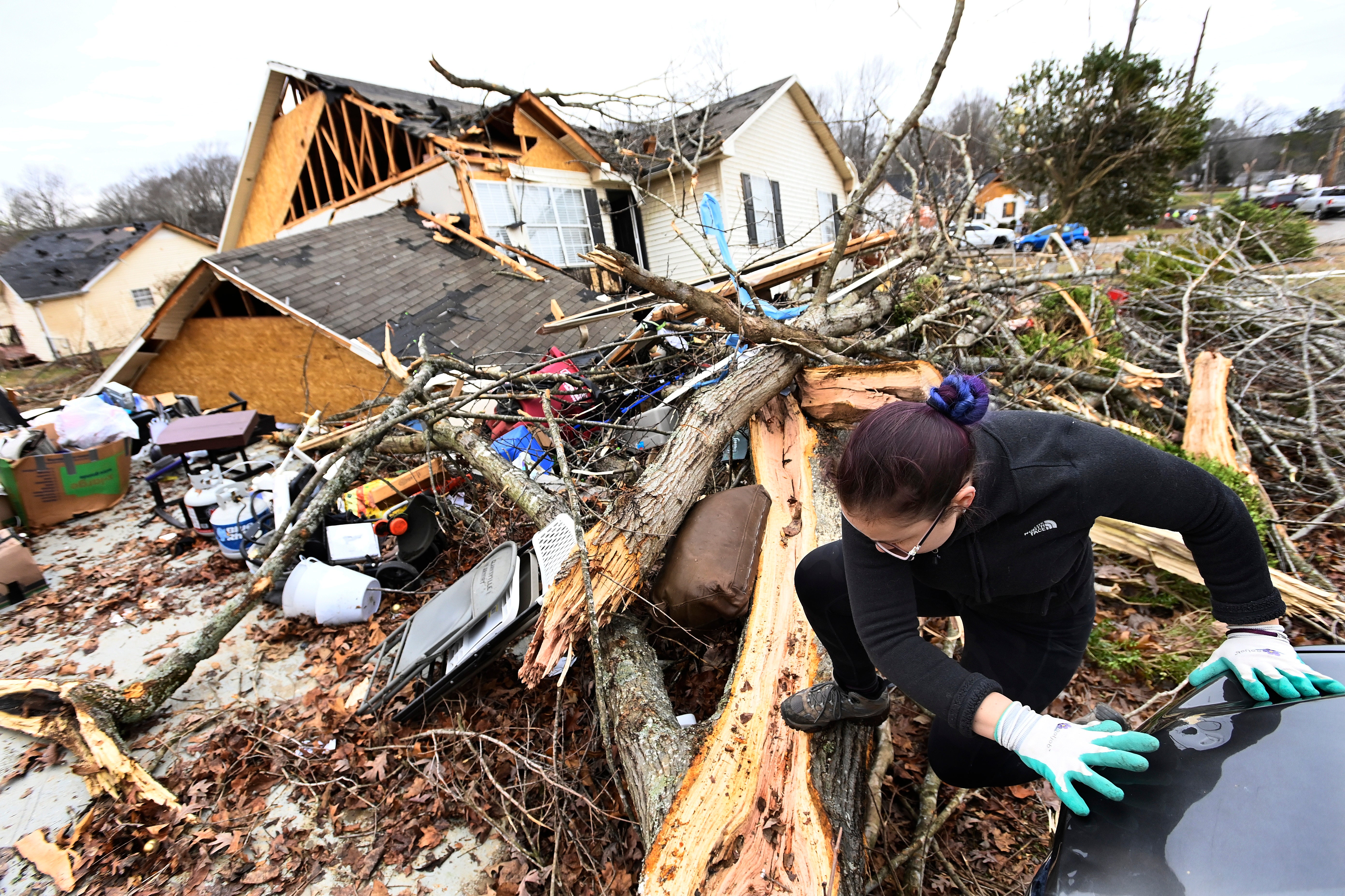 A resident climbs over debris after her friend's home was lifted off its foundation on Sunday