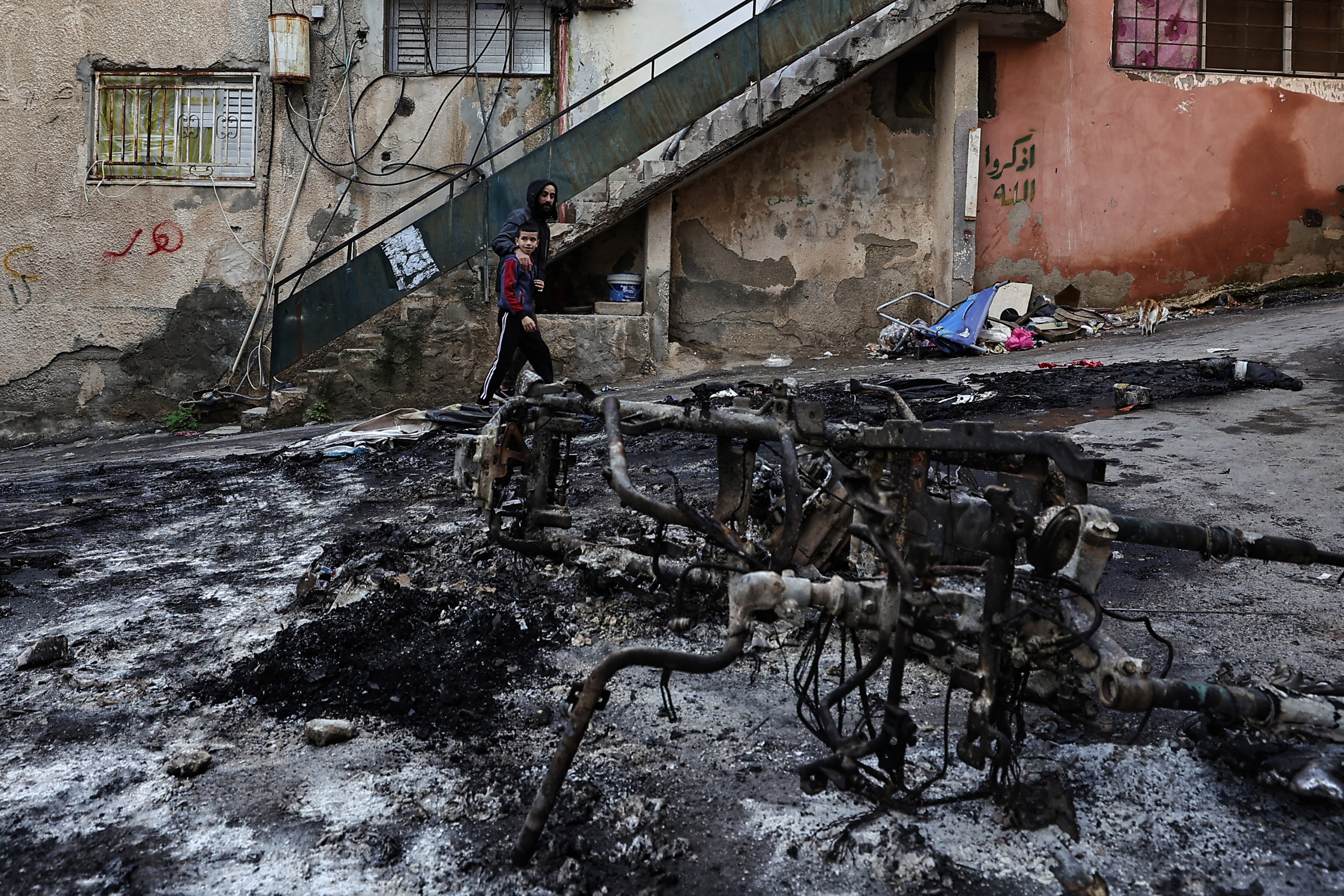 Palestinians walk past a burnt motorcycle following a three-day incursion by the Israeli army on the Jenin camp in the occupied West Bank