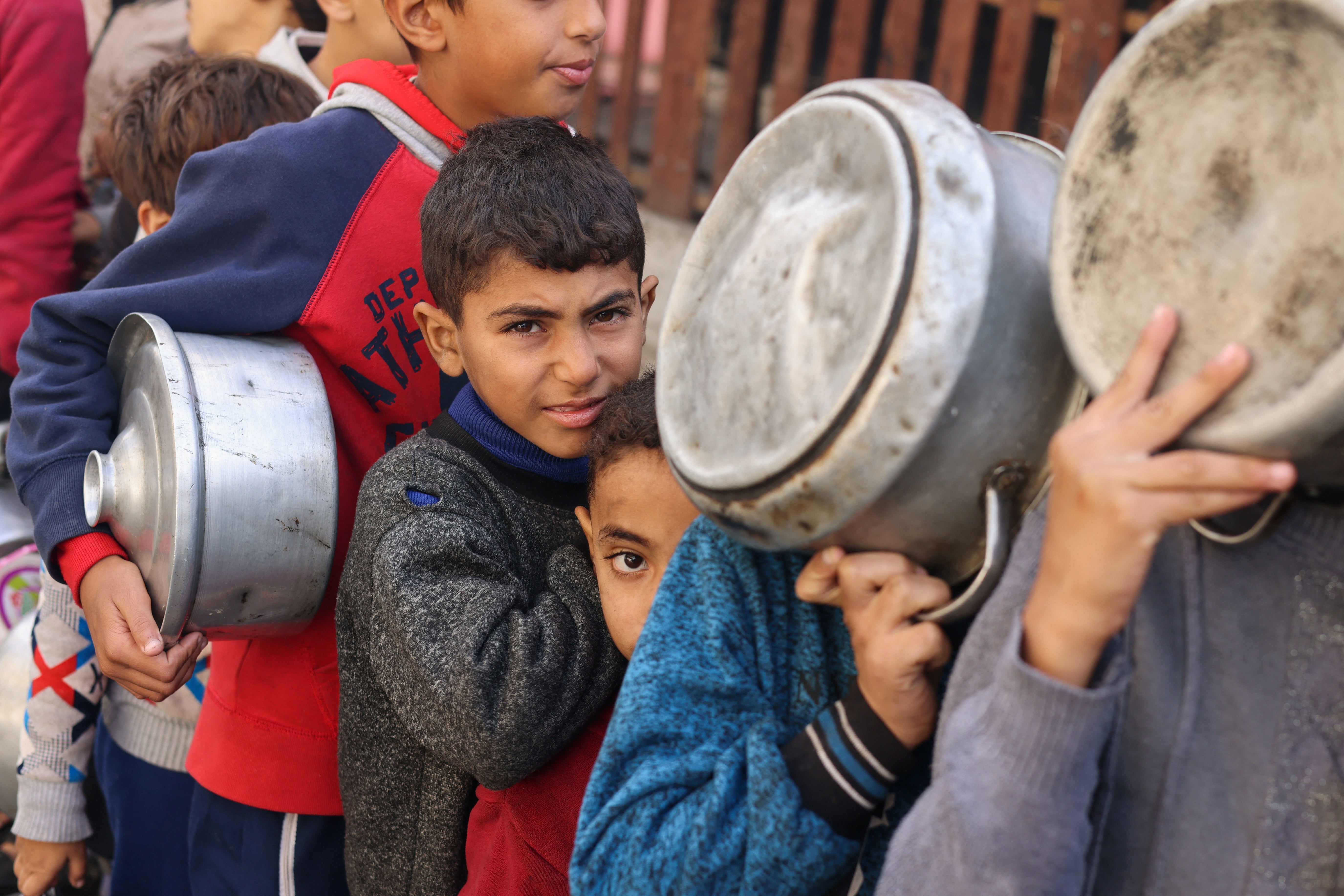 Palestinian children wait to receive food cooked by a charity kitchen in Rafah