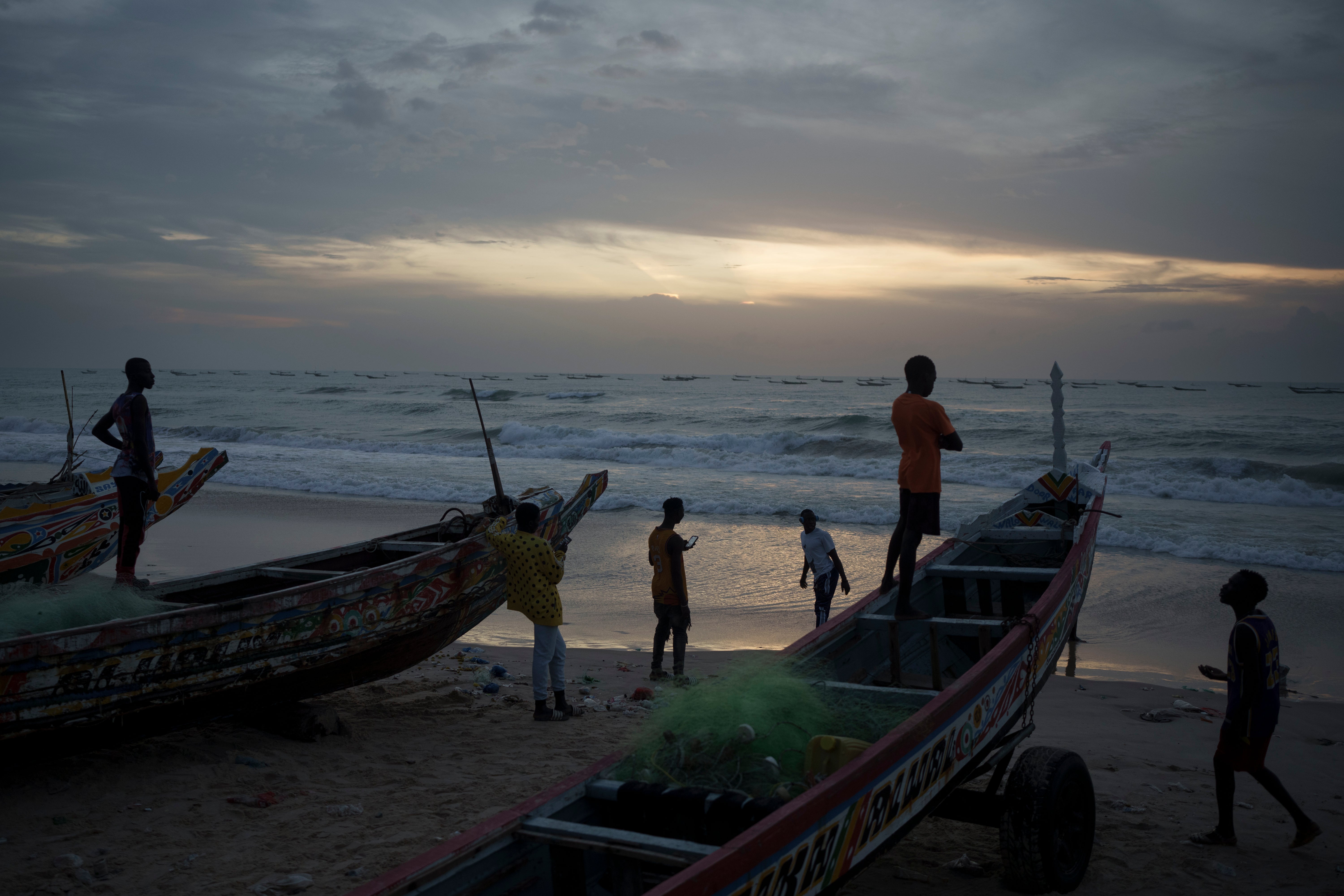 Senegalese youth gather around pirogues on the beach at dusk in Fass Boye, Senegal, Tuesday, Aug. 29, 2023.