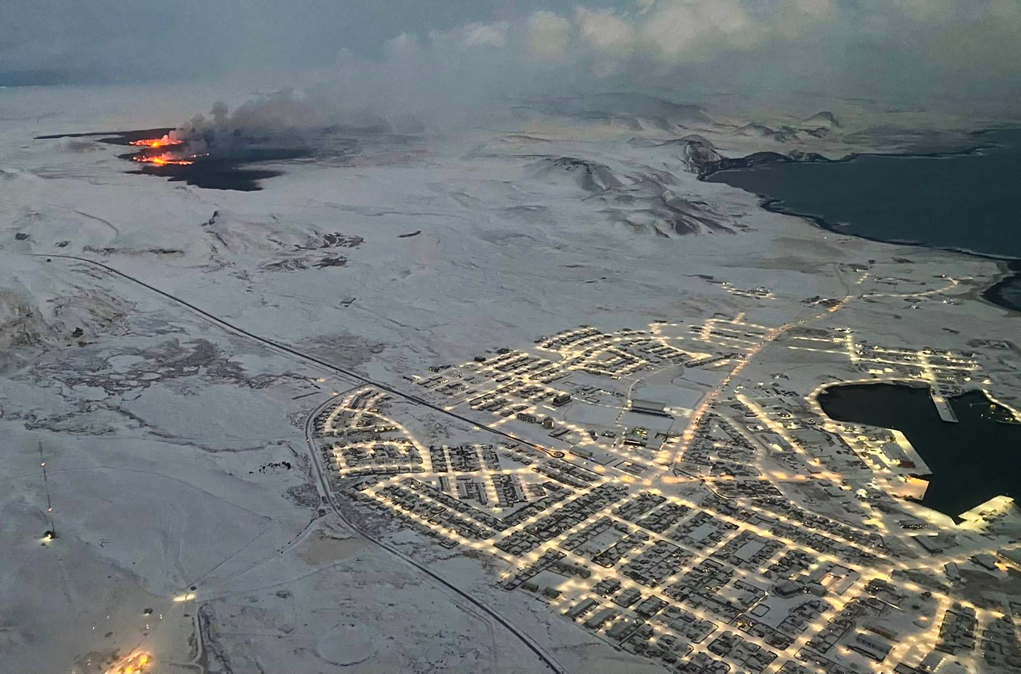 The evacuated Icelandic town of Grindavik (R) is seen as smoke billow and lava is thrown into the air from a fissure