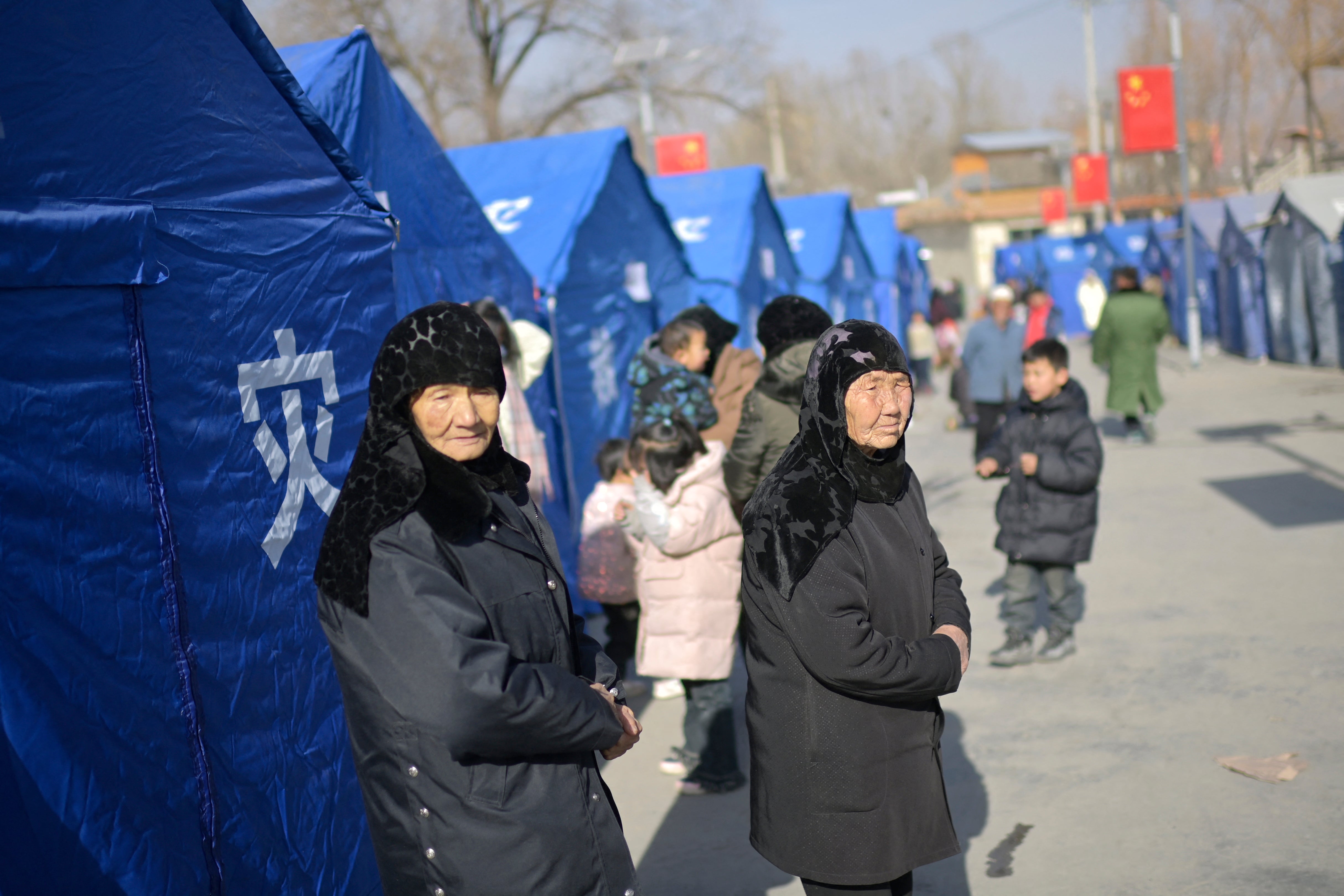 Earthquake-affected residents look on beside aid tents erected in a school compound in the village of Gaoli, in Jishishan