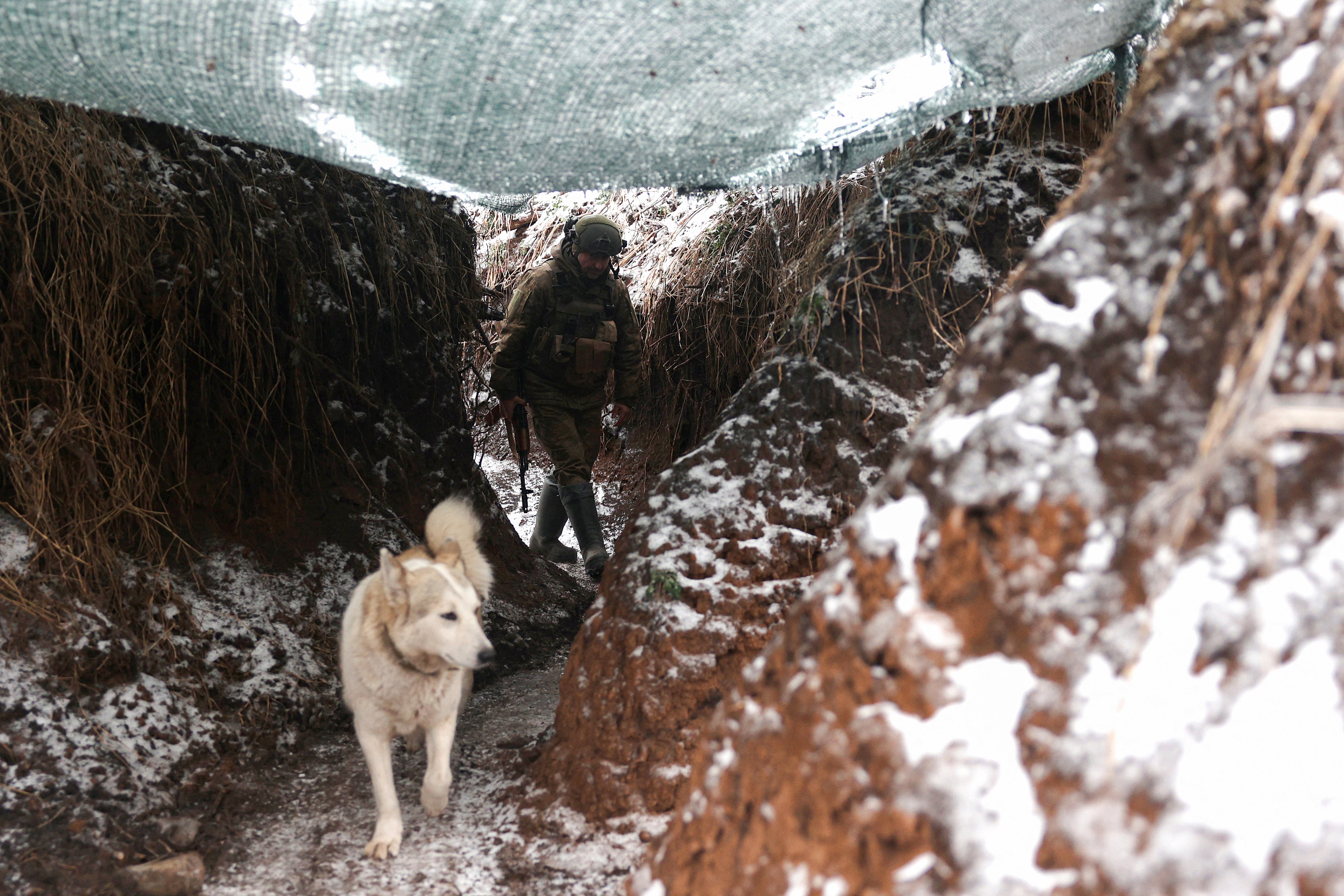 A Ukrainian soldier walks along the trench with a dog as he holds his position at the front line in Donetsk