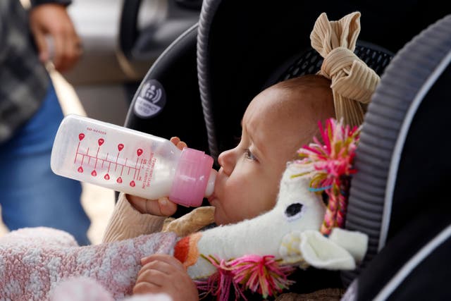 A baby drinks milk from a plastic bottle