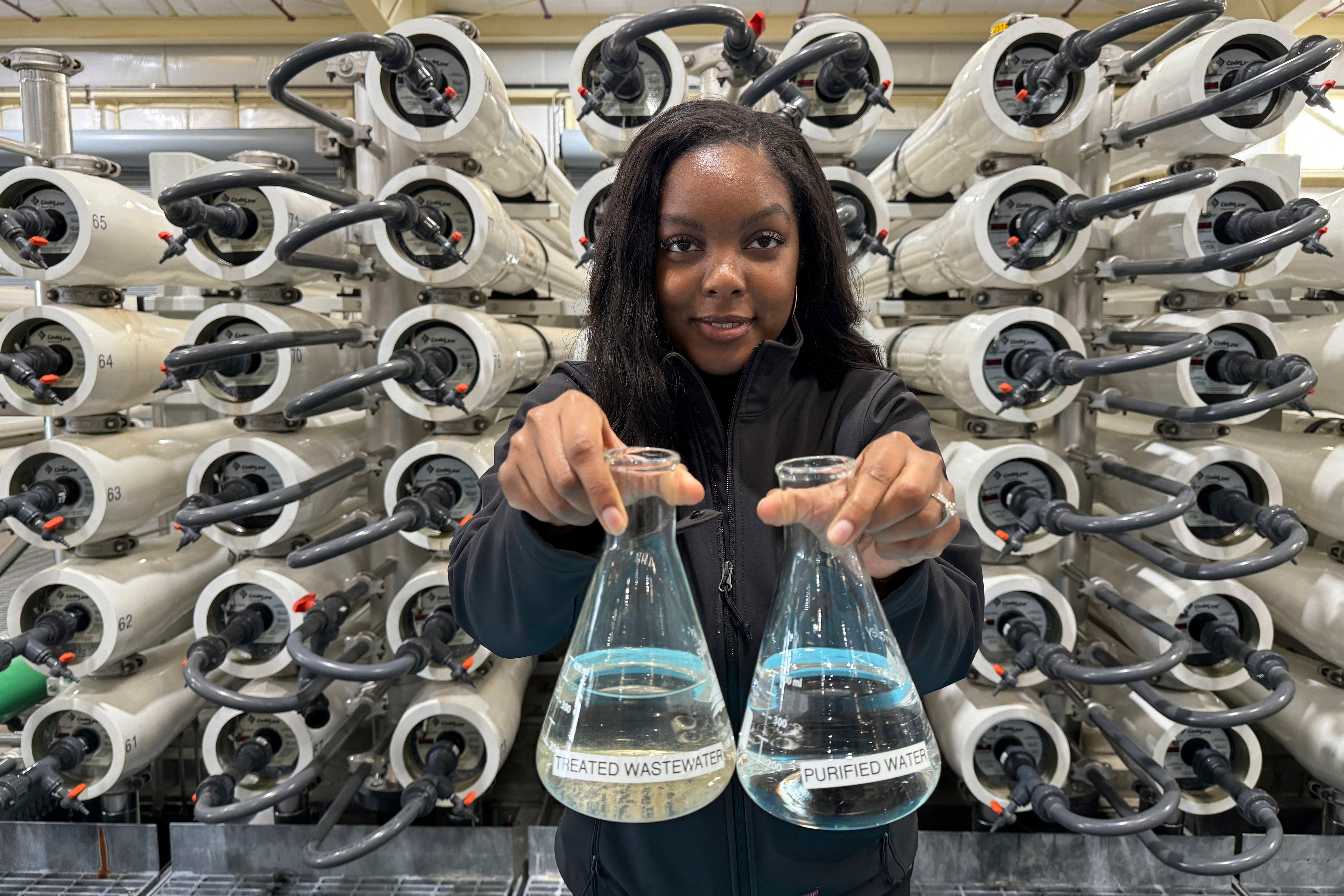Lakeisha Bryant, public information representative at the Santa Clara Valley Water District, holds flasks of water before and after it is purified at the Silicon Valley Advance Purification Center, Wednesday, Dec. 13, 2023, in San Jose, Calif